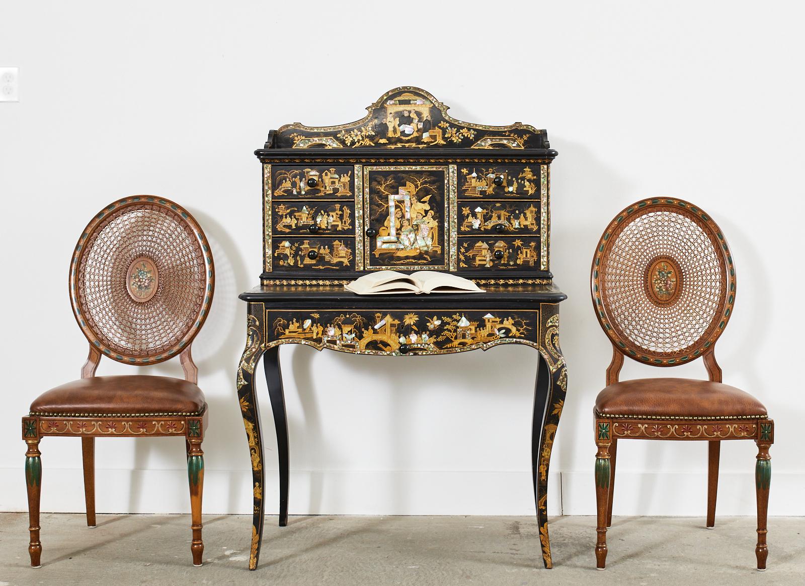 Stunning pair of hand-painted dining chairs decorated in the neoclassical taste by Galimberti Lino in Italy. The chairs feature an oval caned back centered by a medallion with a painted floral spray. The border of the back has delicate bell flowers.