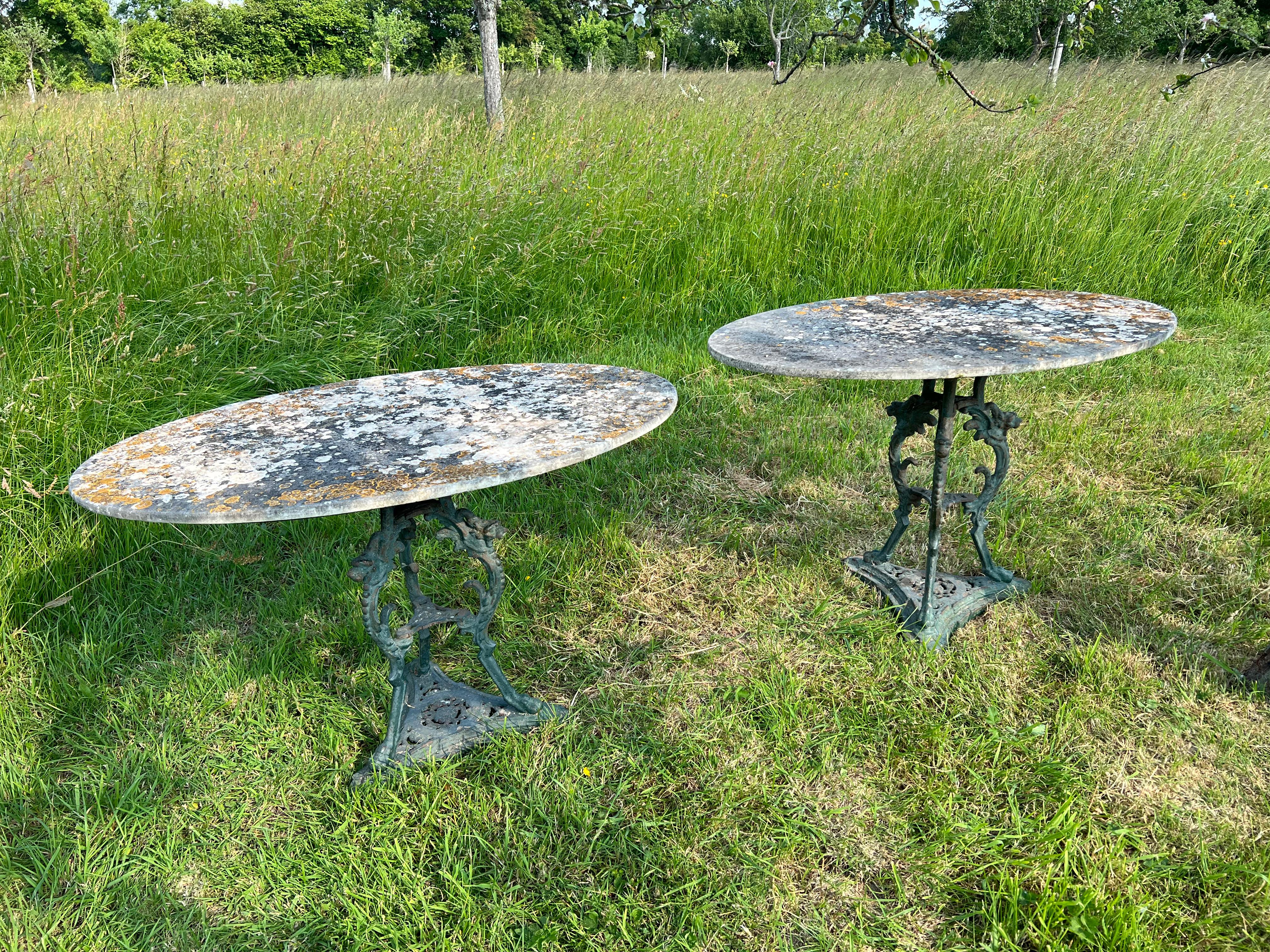 Cette paire de guéridons de jardin présente une élégante forme ovale et incarne l'opulence du style Second Empire. Les pieds en fonte vert-patiné, ornés de motifs complexes de chimères et de têtes de lion, dégagent une impression de grandeur, tandis