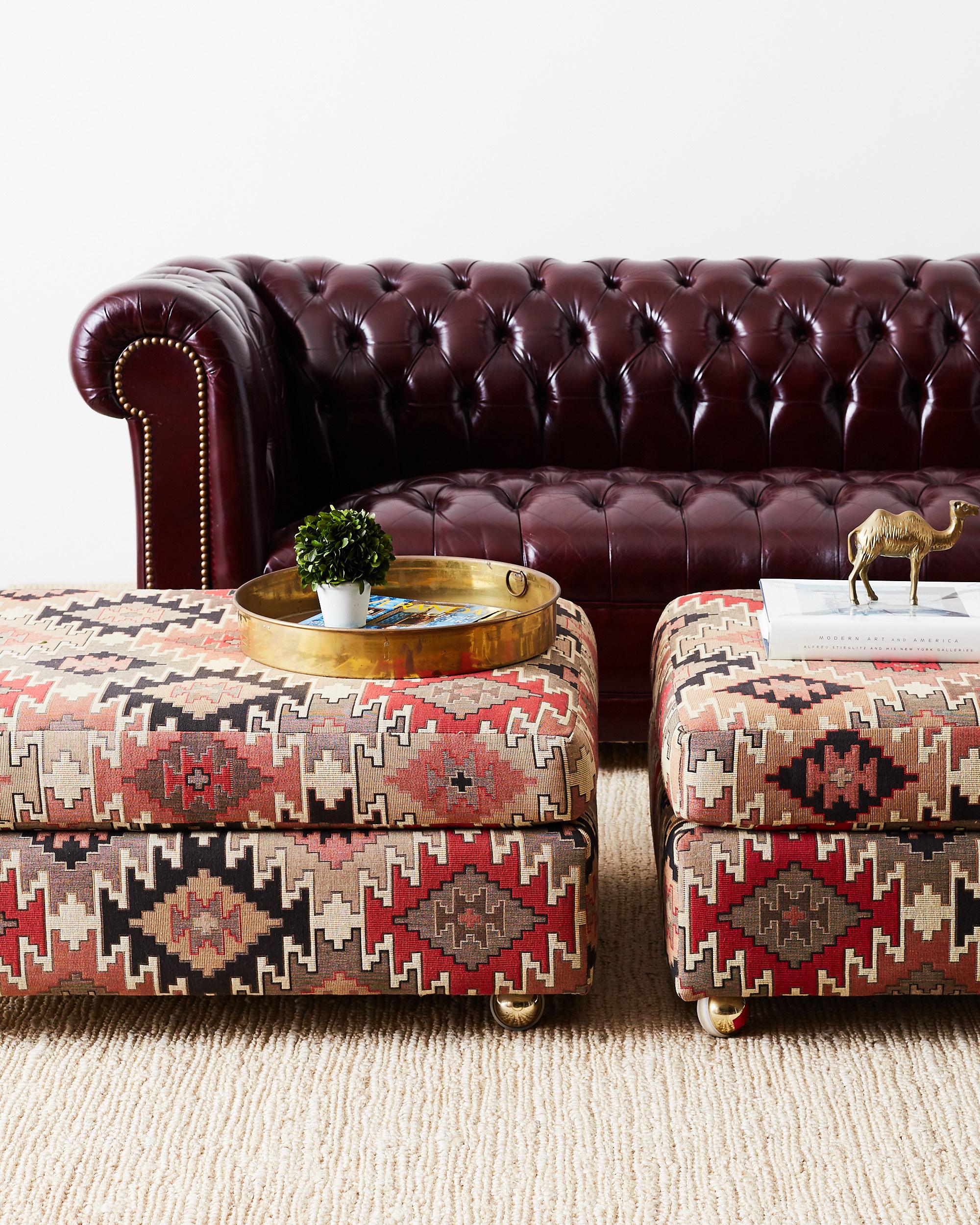 Dazzling pair of upholstered ottomans featuring a Turkish Kilim tribal style fabric. The busy symmetry of the design is reminiscent of a Native American Navajo weave. Beautiful array of red, grey, khaki, salmon and black colors. Fitted over a