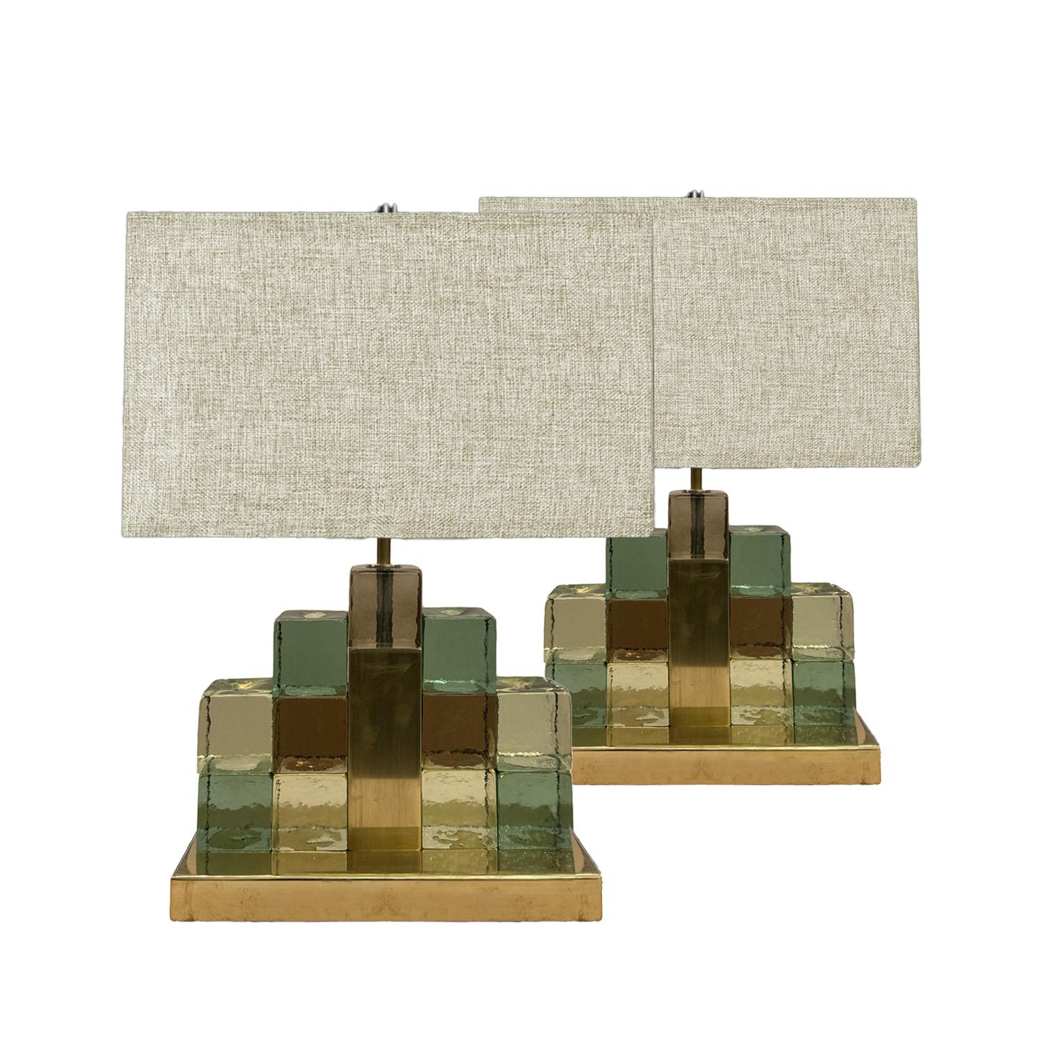 Modern style table lamps with a  geometric design consisting of translucent interlocking Murano glass square blocks in shades of green and gold.  The metallic sheen of the polished brass base compliments the transparent blocks and provides an