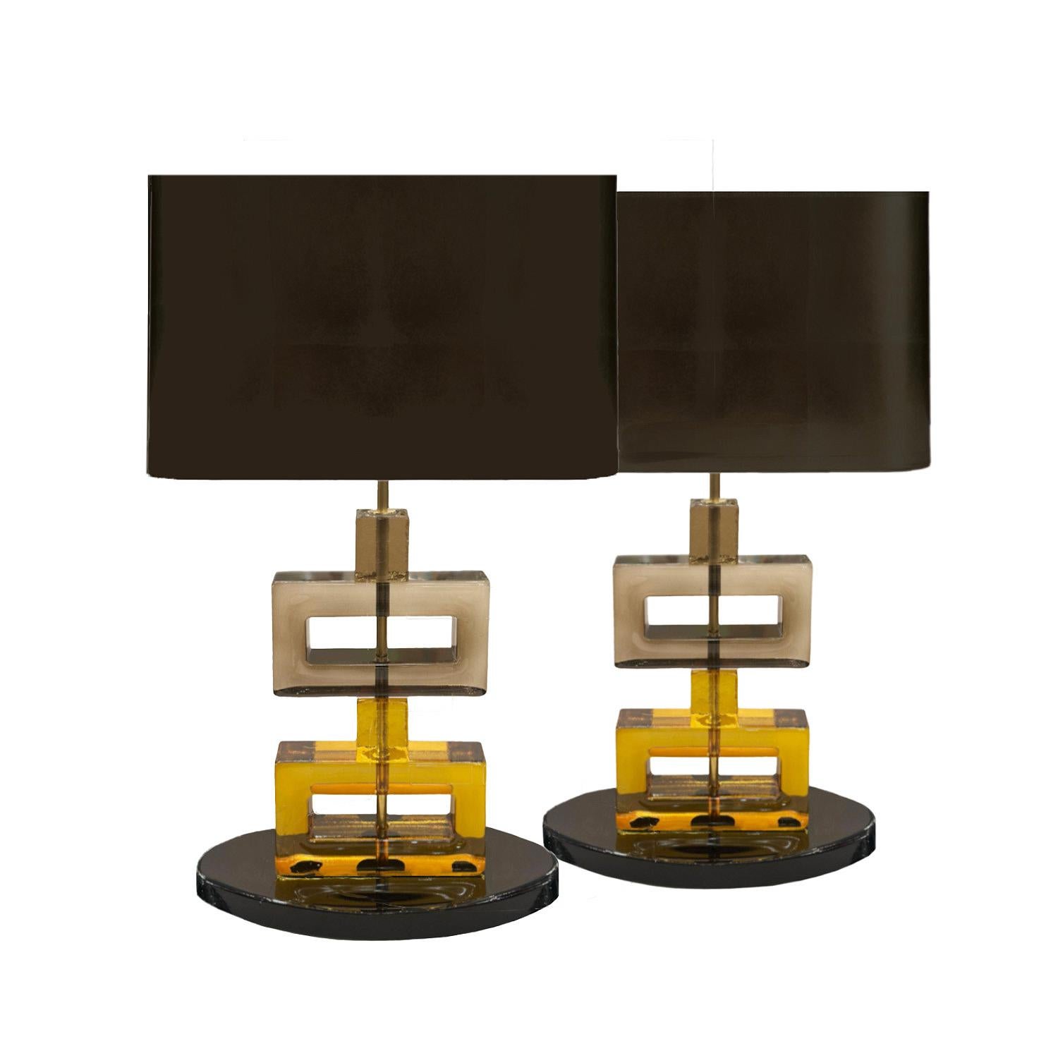 Lampade da tavolo in stile moderno con un caratteristico design geometrico caratterizzato da blocchi di vetro di Murano rettangolari e quadrati impilati verticalmente, traslucidi color fumo e ambra. Una base ovale nera fornisce stabilità e sostiene