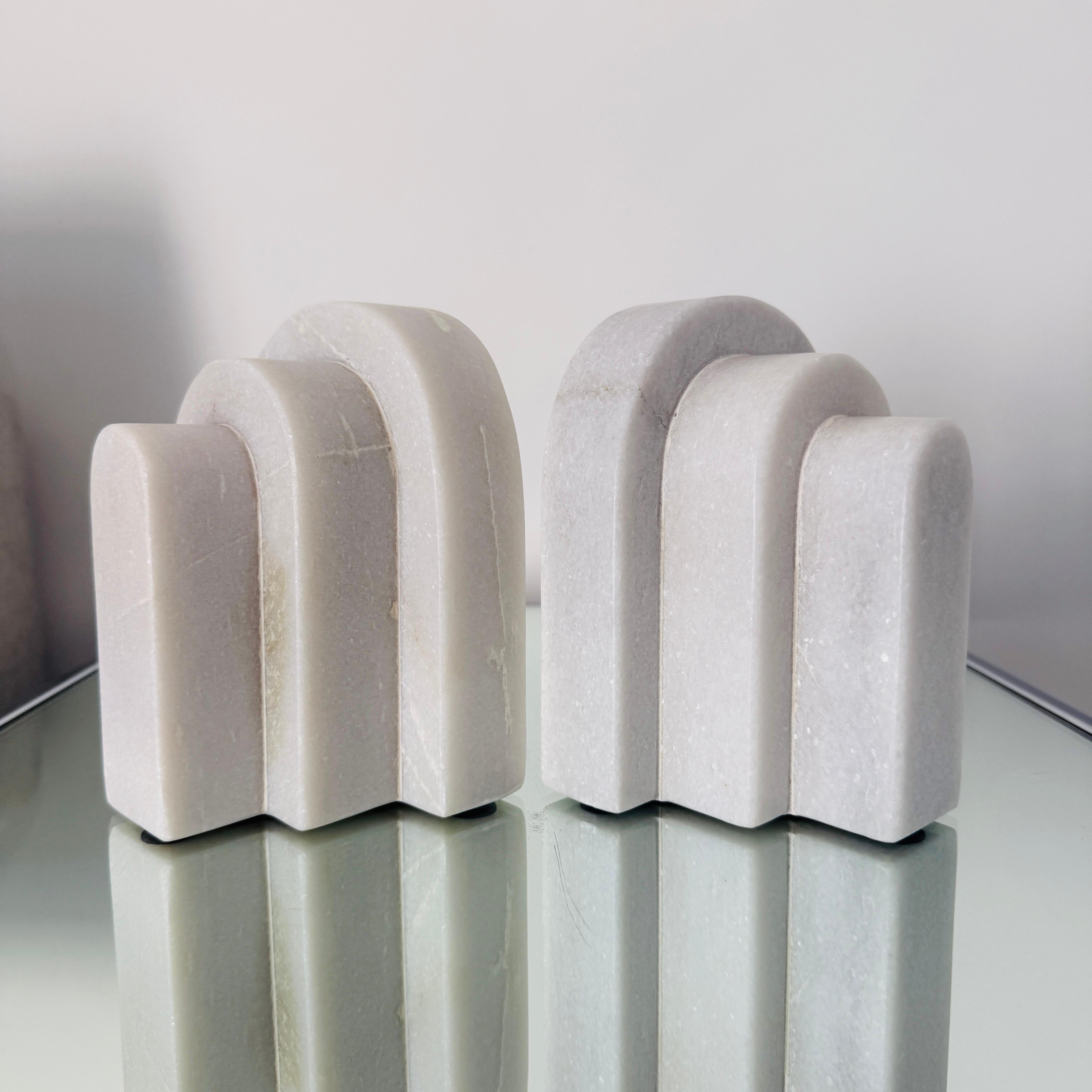 Pair of handcrafted geometric bookends in polished marble.  Unique veining of the marble makes each piece one of a kind.  The bookends have a kinetic design and can be stylized in a variety of arrangements.  Makes a chic desk or bookcase accessory. 