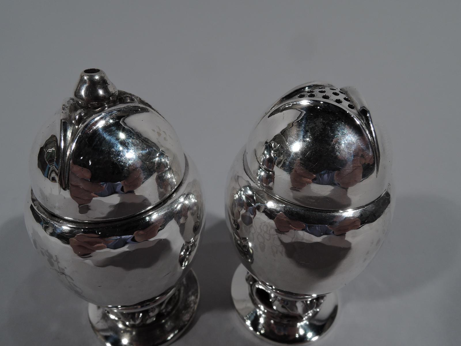 Pair of blossom sterling silver salt and pepper shakers. Made by Georg Jensen in Copenhagen. Each, ovoid on stem with openwork seeded-pod rniceaux mounted to flat and circular foot. Cover comprises 3 leaves with triangular center. One shaker has