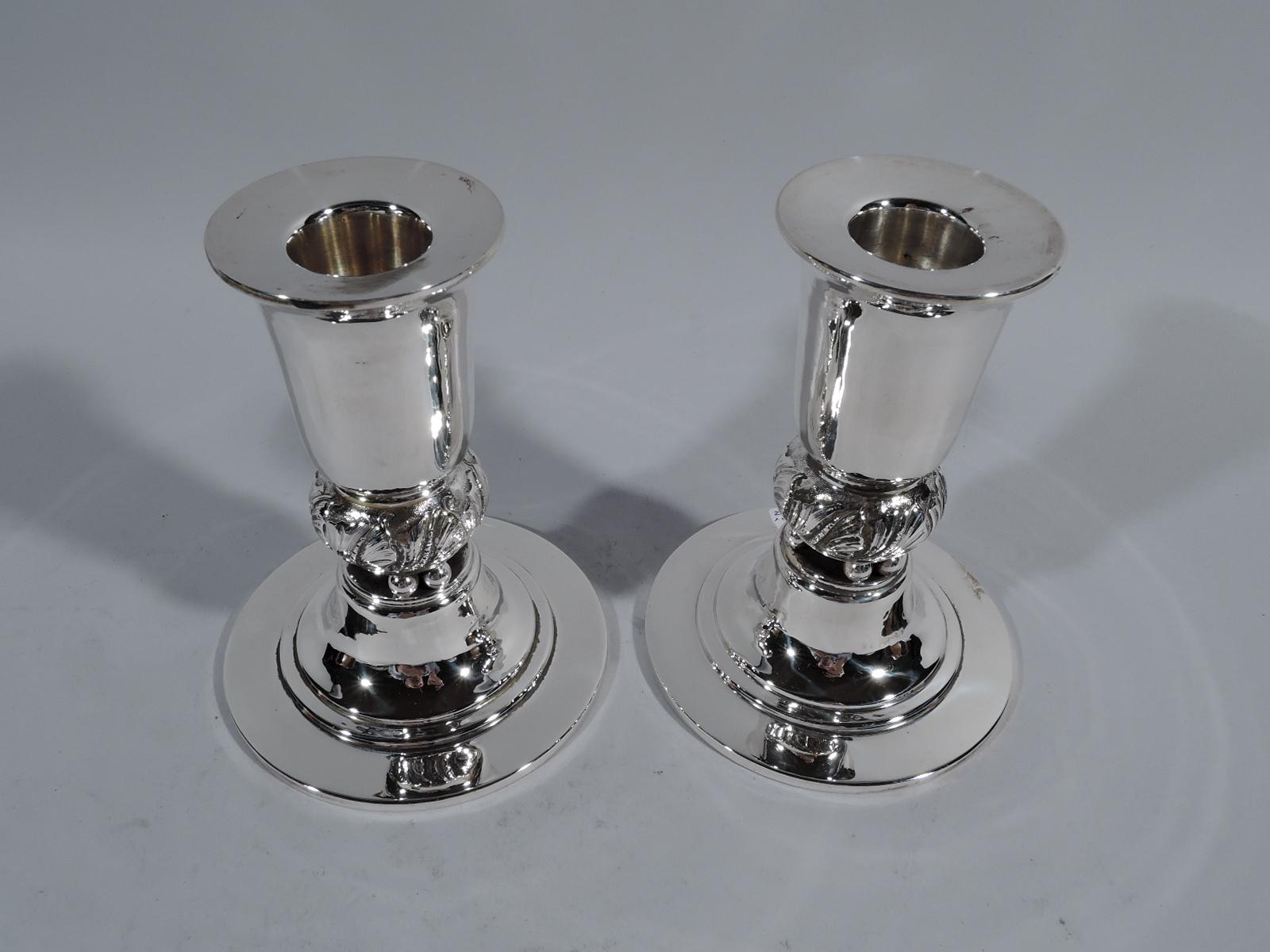 Pair of Mid-Century Modern sterling silver candlesticks. Retailed by Georg Jensen, Inc. USA in New York. Tall urn socket with wide flat rim. Bulbous knop with tooled leaves mounted to beads in turn mounted to stepped and domed foot. Fully marked and