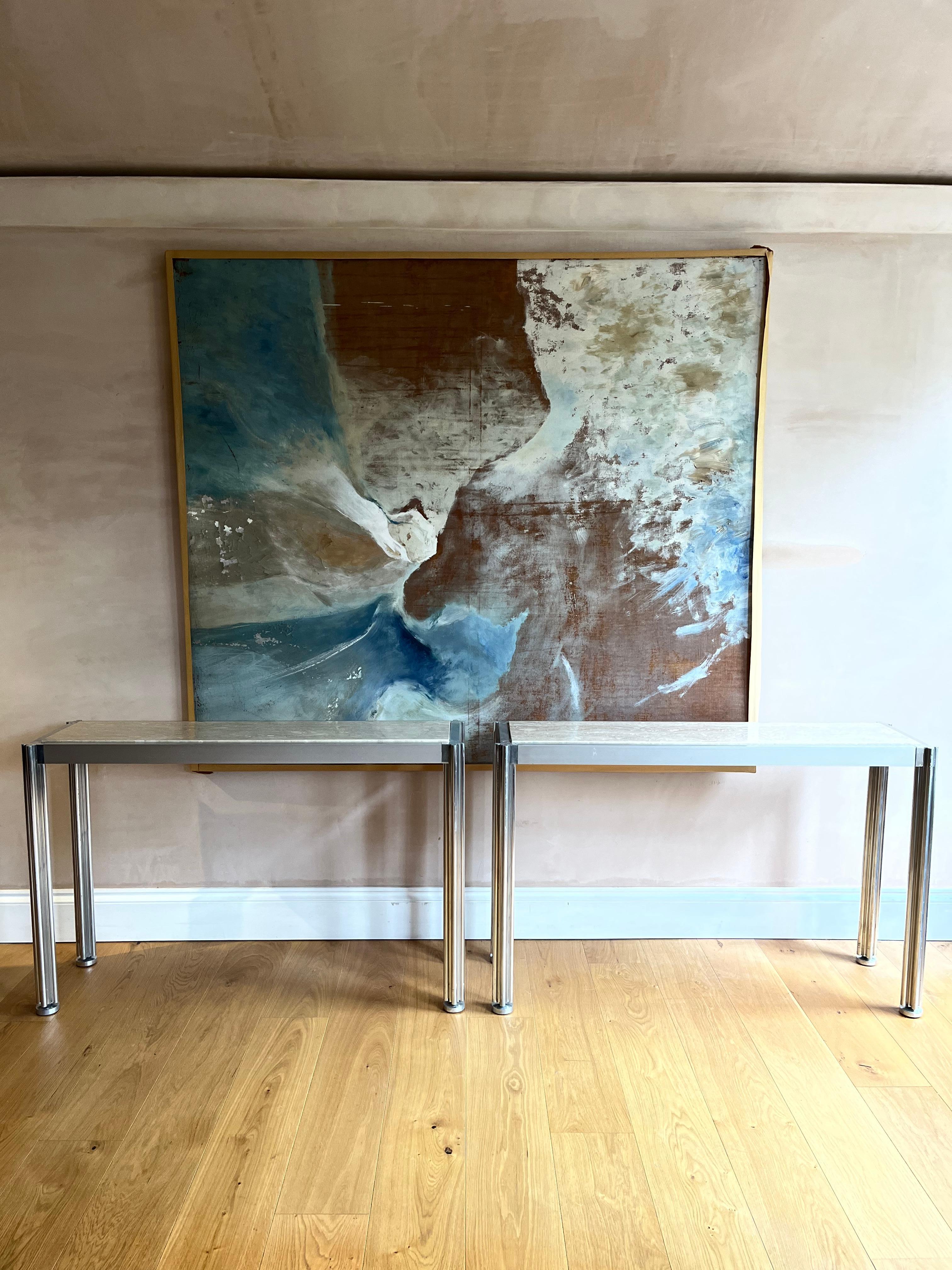 Pair of brushed aluminium and travertine console tables designed by George Ciancimino. One back corner leg has been cut down possibly to fit into a restrictive space. There is a also some distortion to the top of one of the back bars and there are