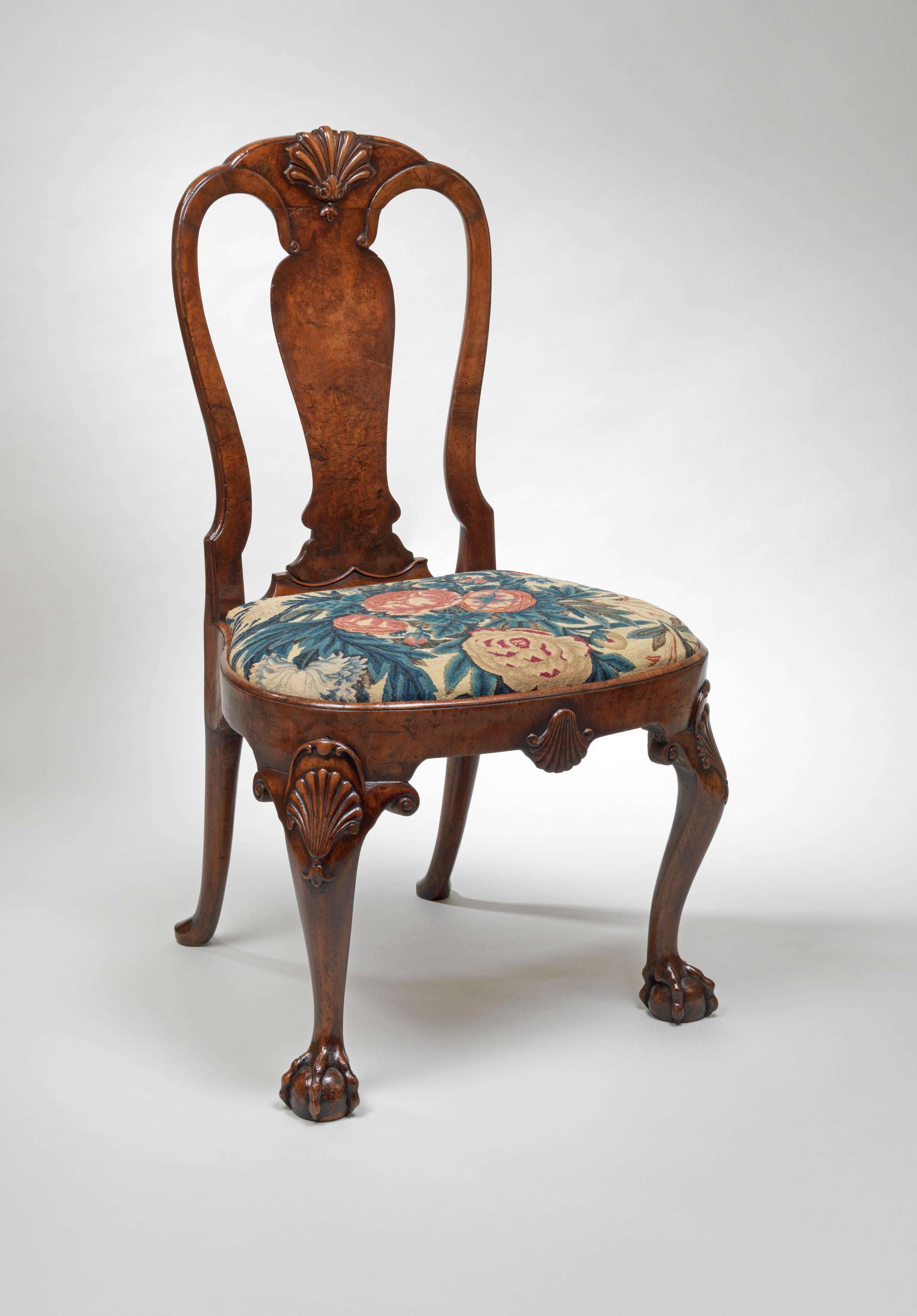 Each chair has a gently curving top rail carved with a central shell and foliage; the tops of the sinuous side rails curve round to join the top of the wide inverted baluster splat. The front rail of the seat is carved with a shell, as are the