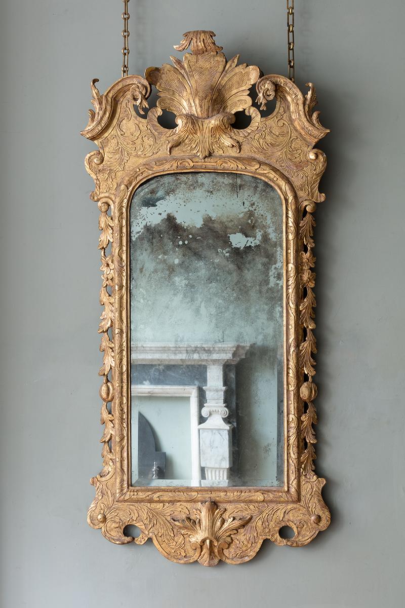 The giltwood frame with a soft lustre, each having scroll arched pediment, centred by a pronounced shell with acanthus decoration above the original bevelled plates within a foliate scroll punched strapwork ground. The shaped apron centred by a
