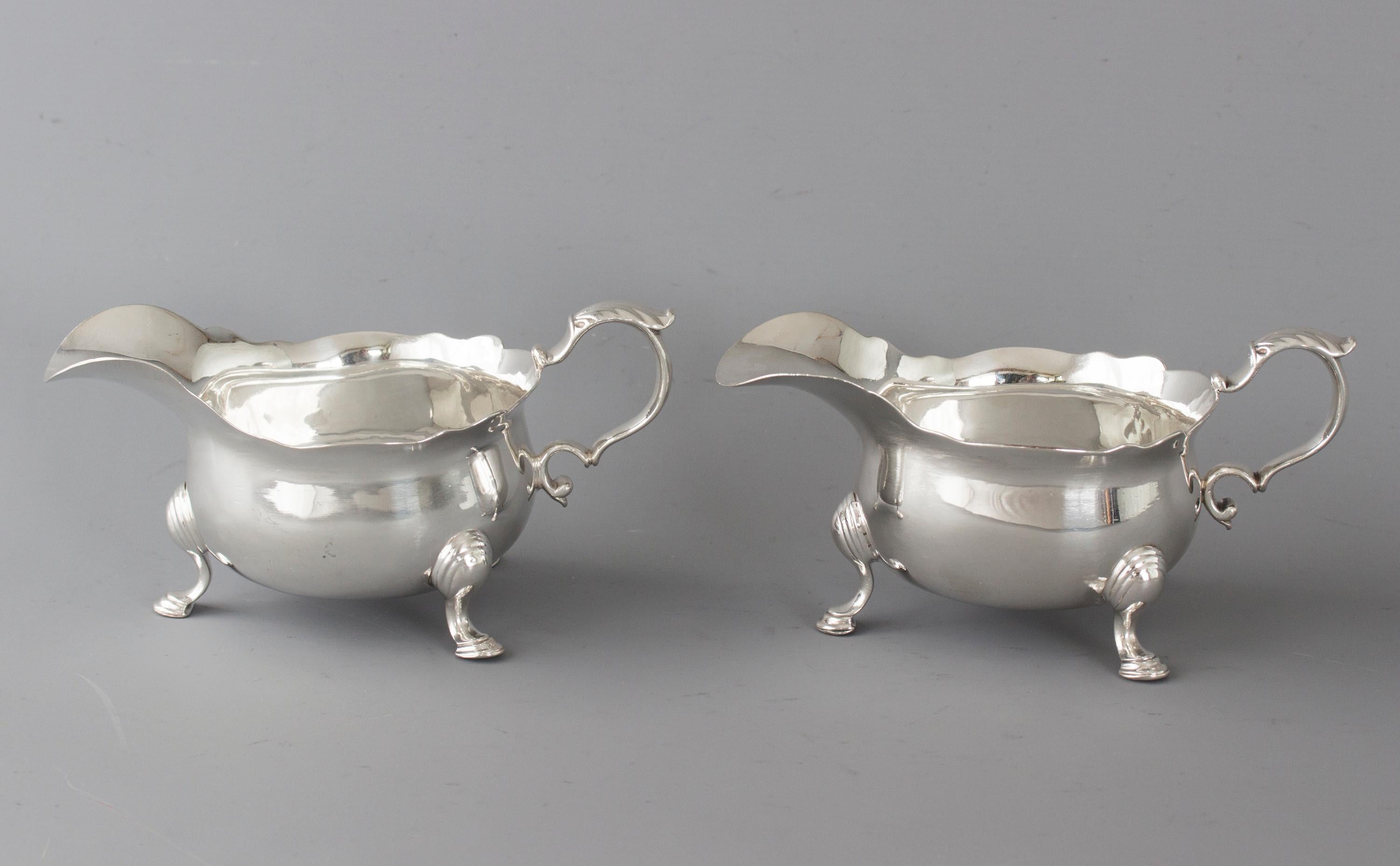 These superb silver sauce boats are of the raised circular form with extended pouring lip and applied handle surmounted with a cast acanthus leaf thumbpiece. The body bellied with a cut wavy rim. All standing on three cast legs decorated with hoof