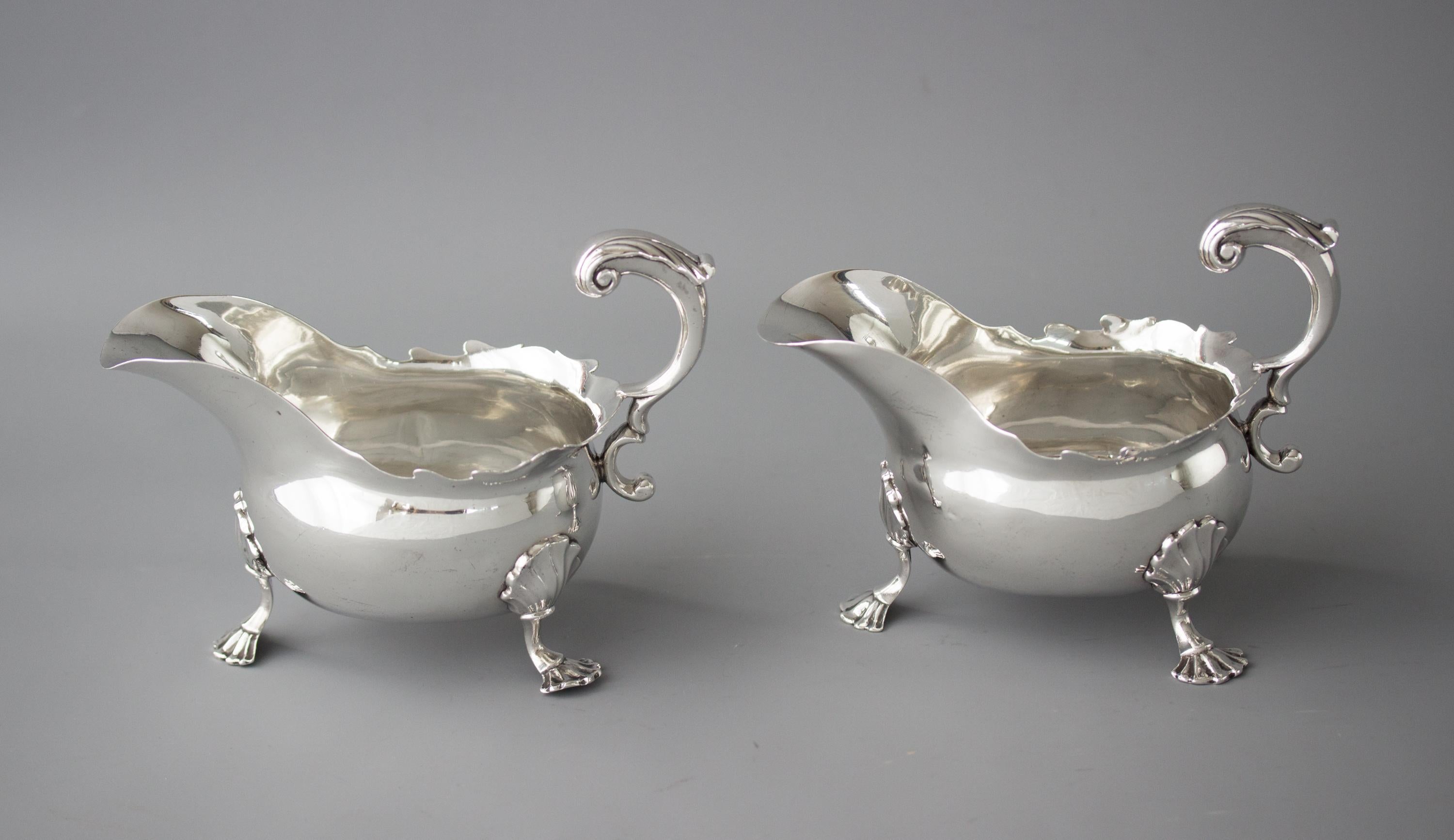 An exceptionally fine pair of large silver sauce boats with a cut card rim and a flying C-scroll handle. Each standing on three shell formed legs and shell pad feet. 

Both marked to the underside for London 1752 by David Bell and Richard Mills.