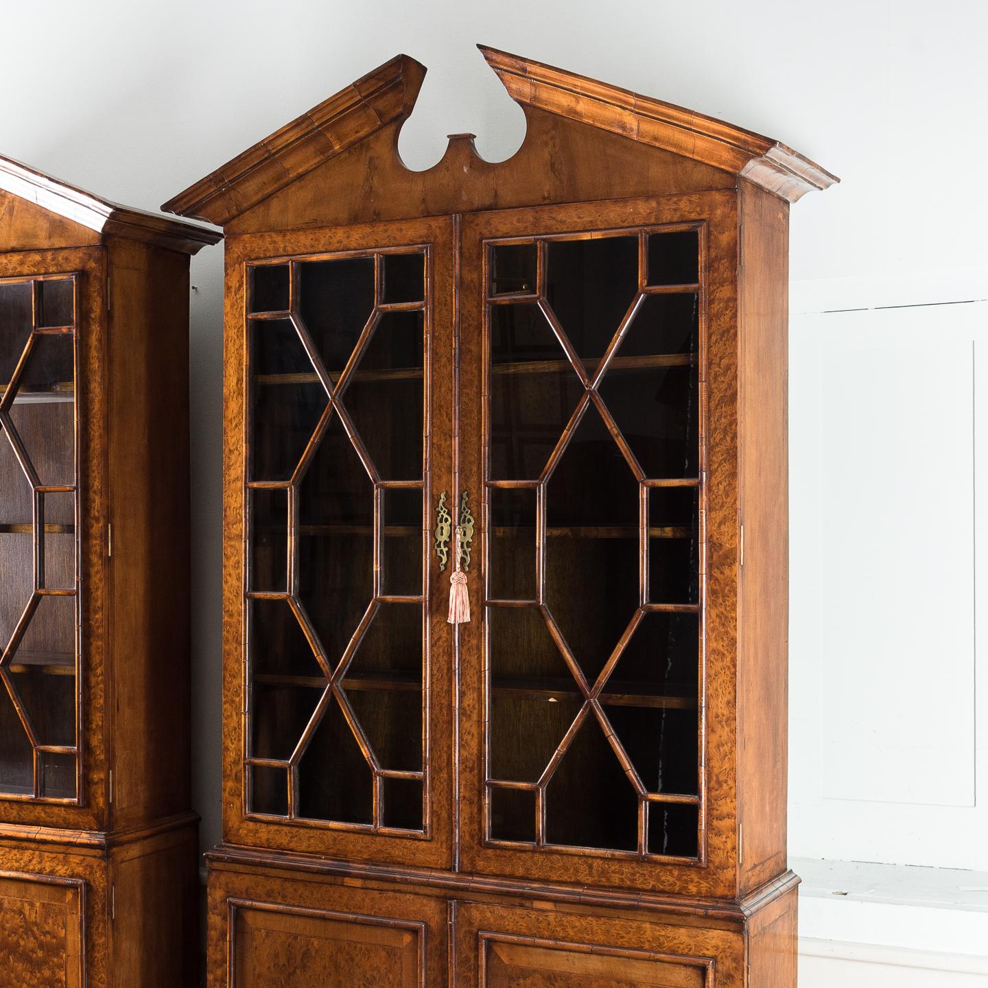 A pair of George II style burr yew bookcases, mid-20th century, each with bold architectural broken pediment above a pair of astragal glazed doors, the base with crossbanded and strung doors, on bracket feet, the interiors containing shelving.