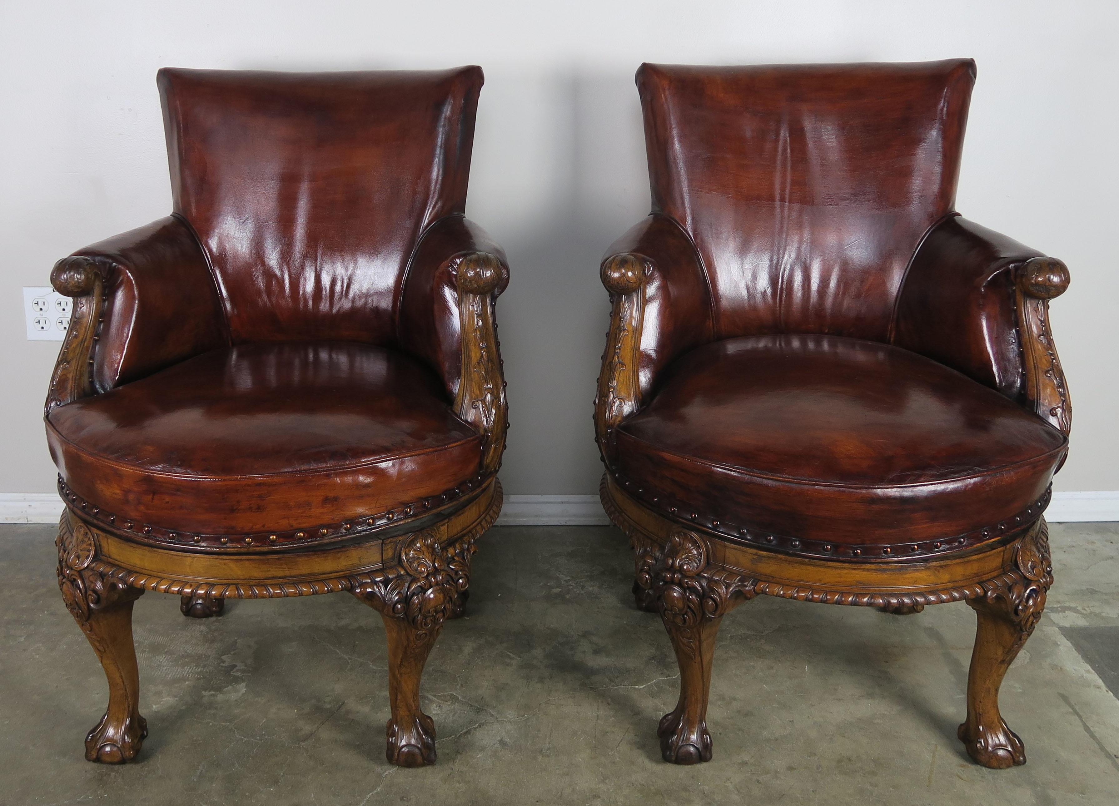 Pair of English George II style walnut swivel library chairs upholstered in original rich cognac colored leather with leather gimp and spaced nailhead trim detail. The chairs stand on four beautifully carved legs ending in ball and claw