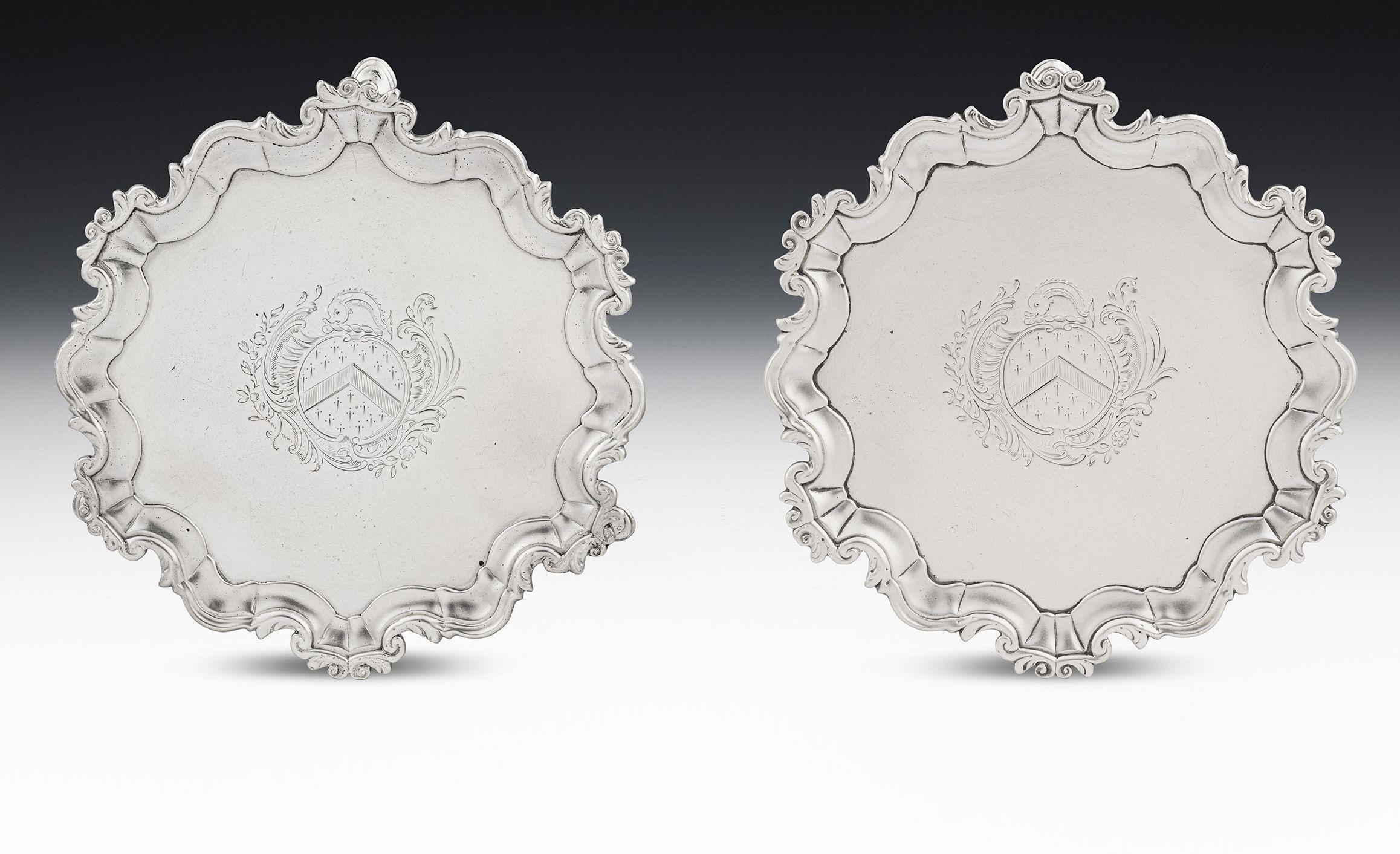 A Rare Pair of George II Waiters or Bottle Stands Made in Dublin circa 1755 by James Warren.

The Waiters are of an unusual size and stand on three hoof feet. The raised scroll border is decorated with foliate motifs and the centre of each piece is