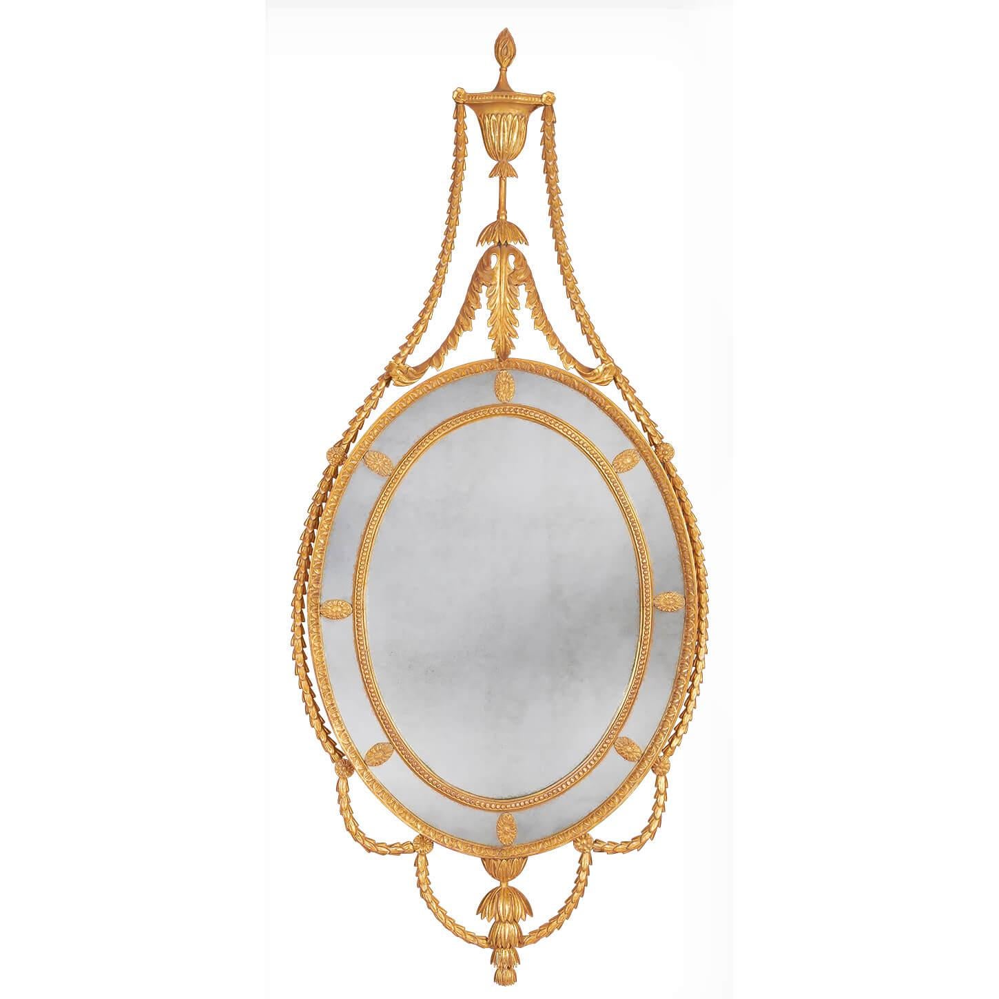 A pair of carved giltwood George III mirrors of Adam design with leaf carved outer frame and bead carved inner frame, the surrounding border glasses are punctuated by oval flower-head paterae. The cresting formed of a classical urn. The flame finial
