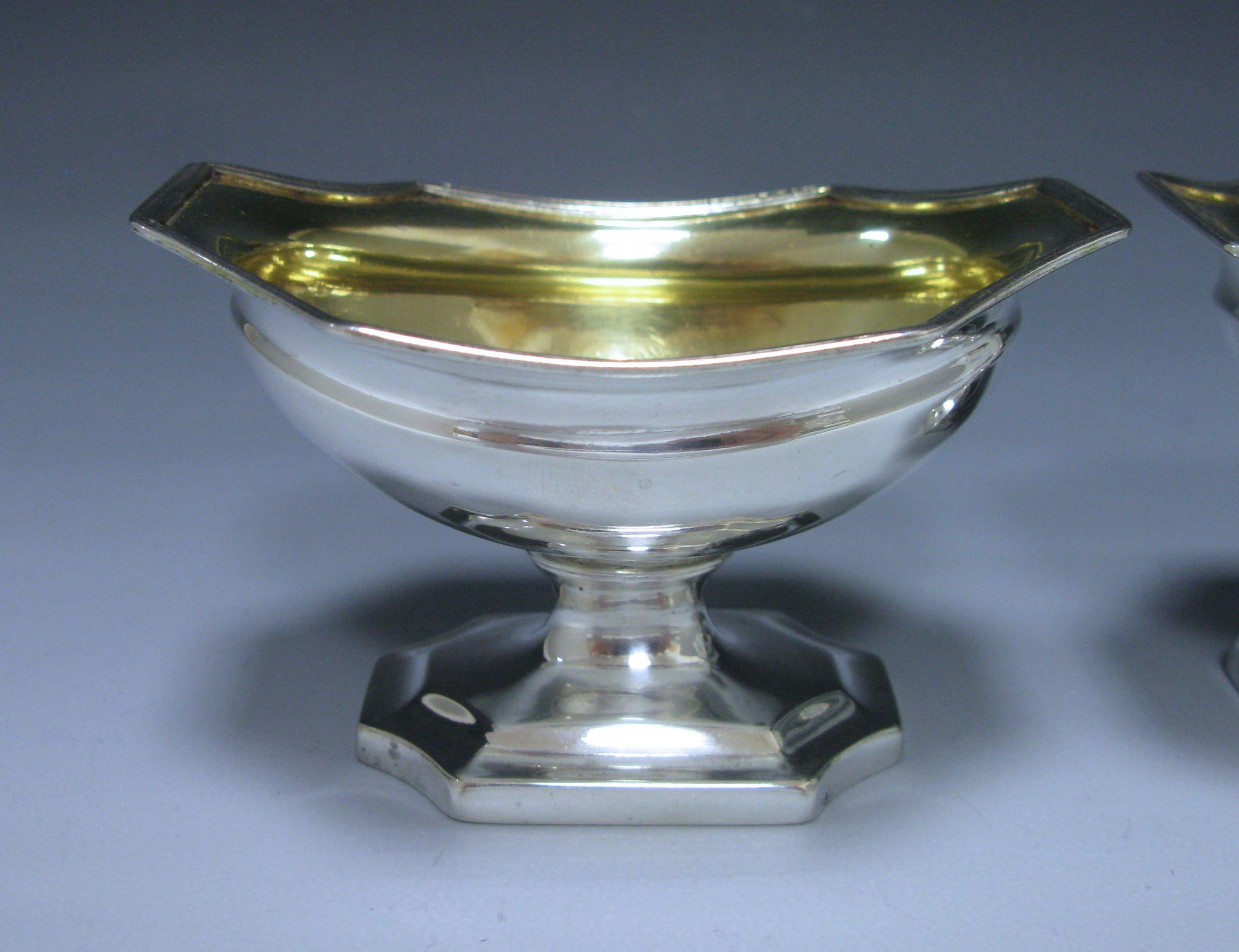 A delightful pair of George III antique silver salts which are of oval shaped form with shaped octagonal borders. The bodies are plain and unembellished, they also stand on shaped oval pedestal bases. The interiors have the original gilding. By