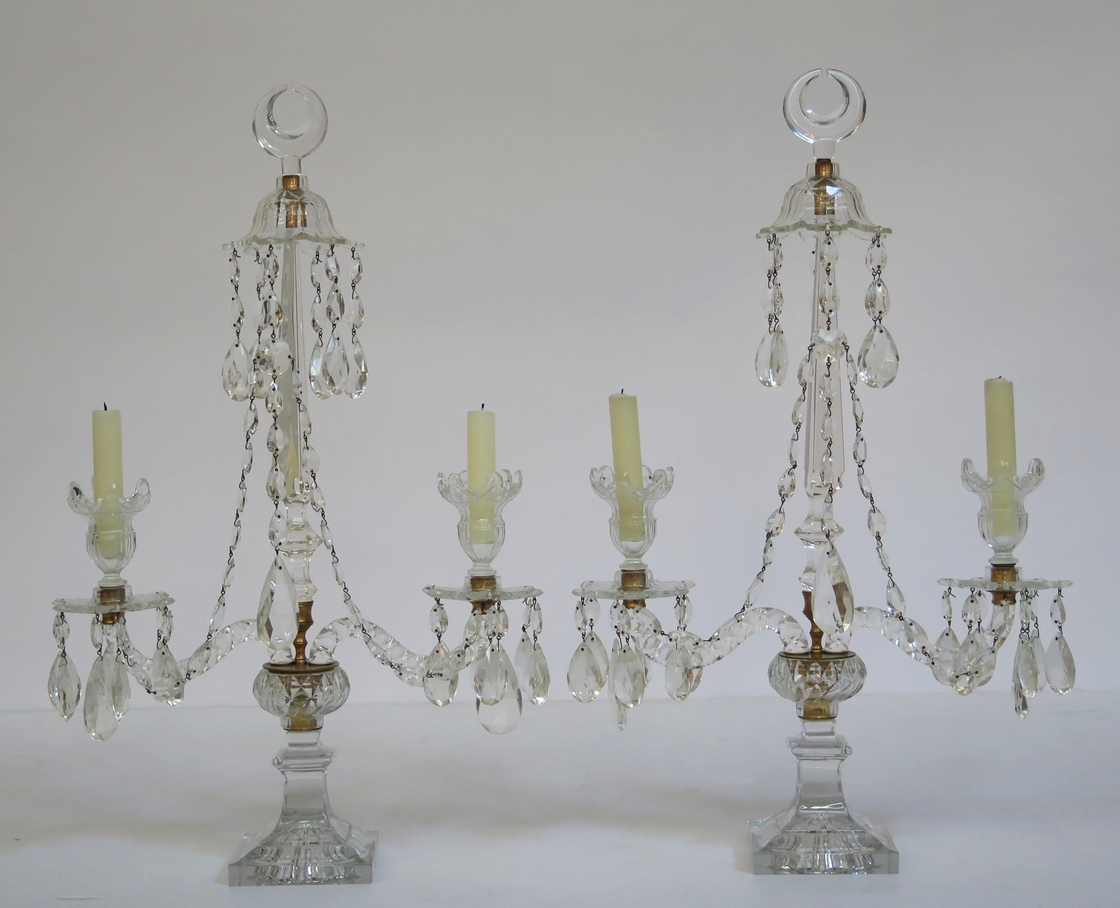 A pair of George III crystal and gilt bronze mounted two-light candelabra. Each has a pair of typical scrolling form arms, and a central tapering spire. The candle arms are united by strings of pear shaped drops around the central spire which is