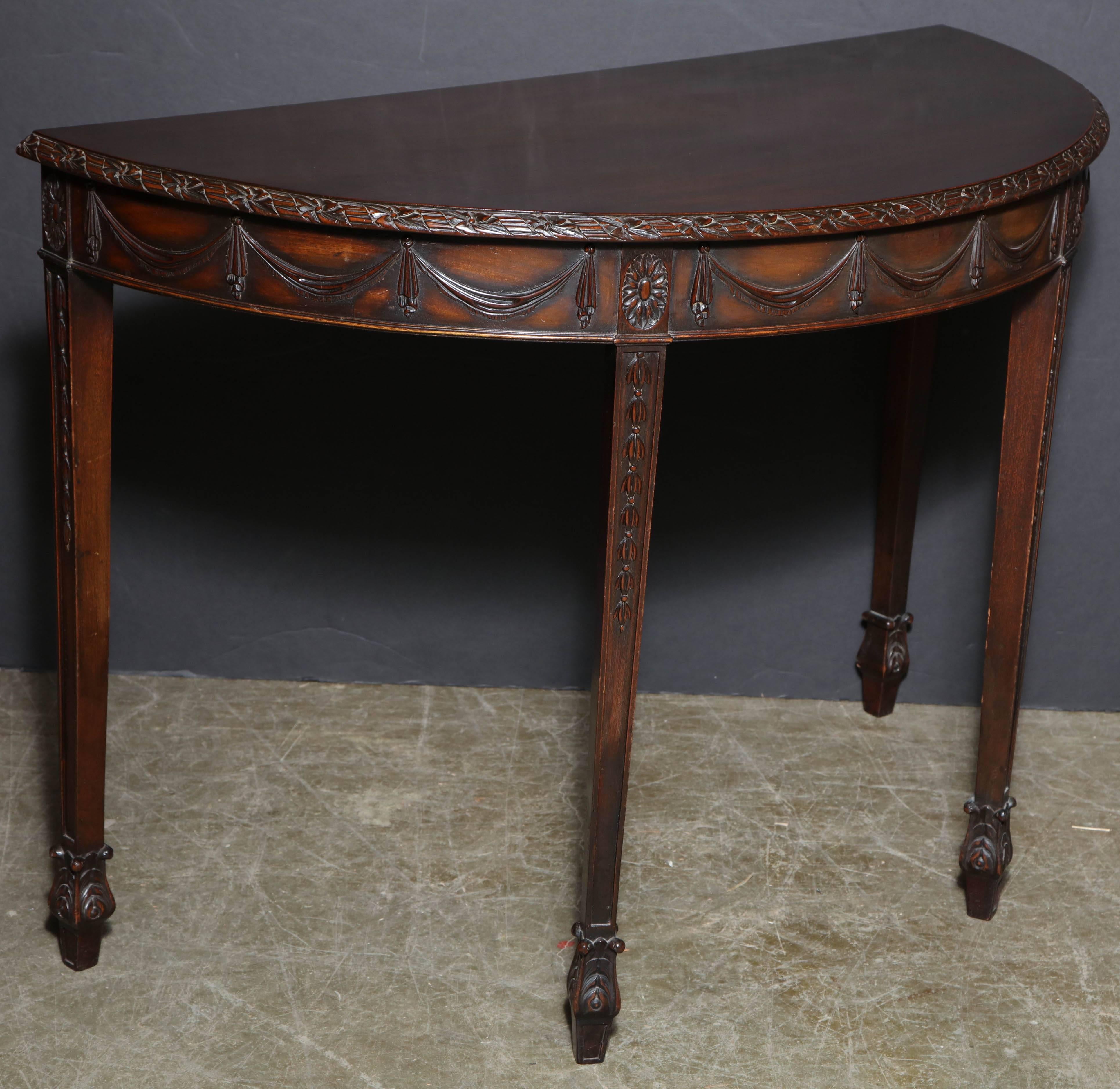Pair of English George III carved mahogany demilune console table with ribbon and blossom edge, drapery carved aprons, carved bell flower tapered legs on unusual spade feet.