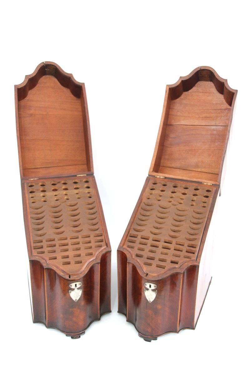 Pair of George III figured mahogany inlaid cutlery boxes each with serpentine fronts and inlaid edges. Each possesses silver mounts opening to inserts above a conforming case ending in a beaded edge and raised on flattened ogee bracket feet. Inserts