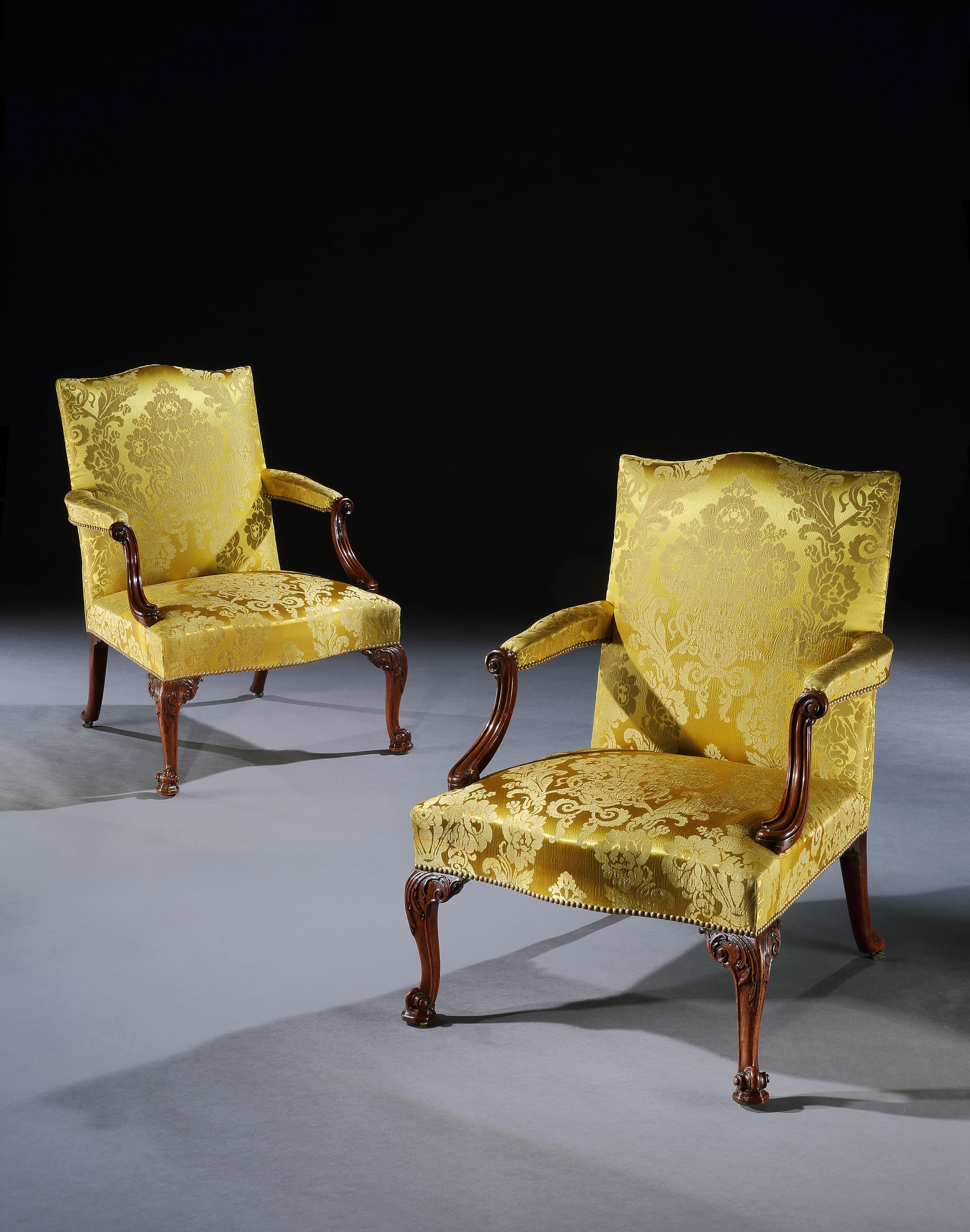 A fine pair of early George III Gainsborough open arm chairs in well carved mahogany of excellent colour and patina, covered in a gold silk damask and with carved shaped arms, standing on cabriole legs carved with acanthus and terminating in a