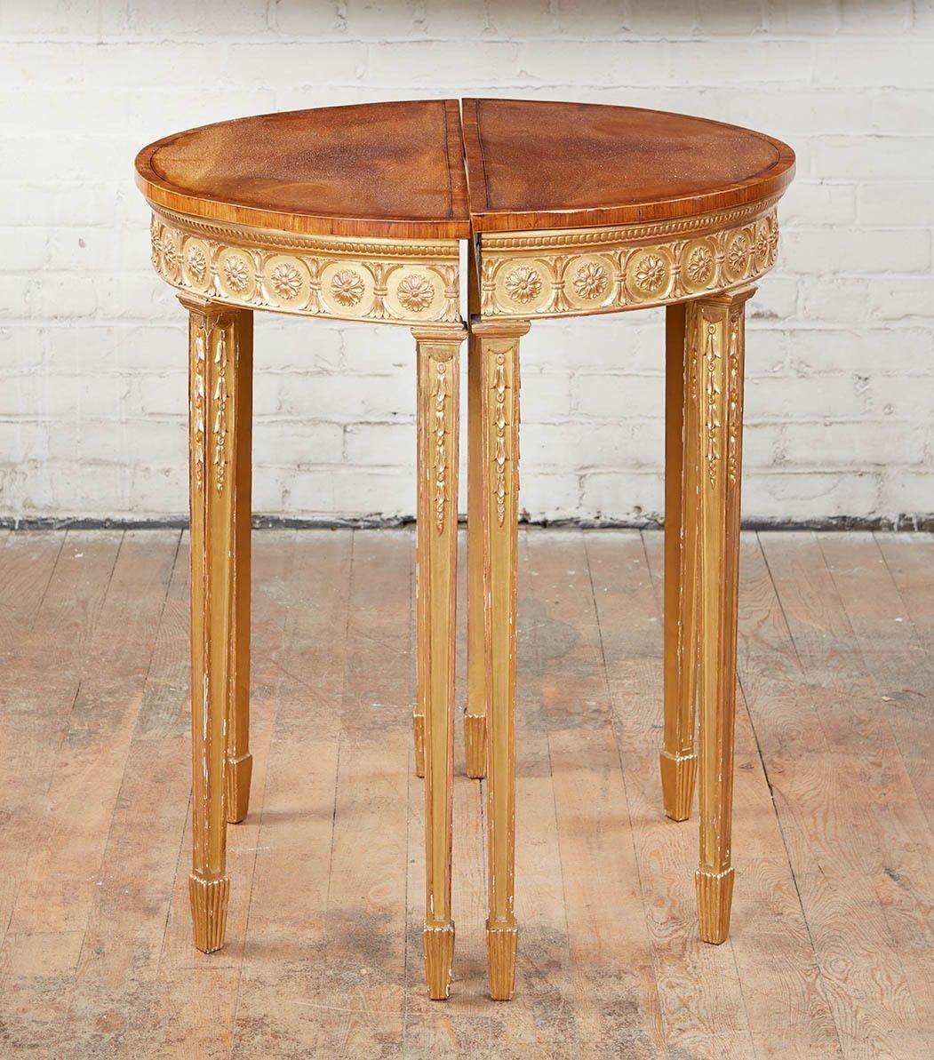 Fine pair of George III demilune console tables having mahogany tops cross banded with kingwood, over gilt wood base having rosette decorated apron and standing on square tapered legs having carved bellflowers and standing on fluted spade feet.