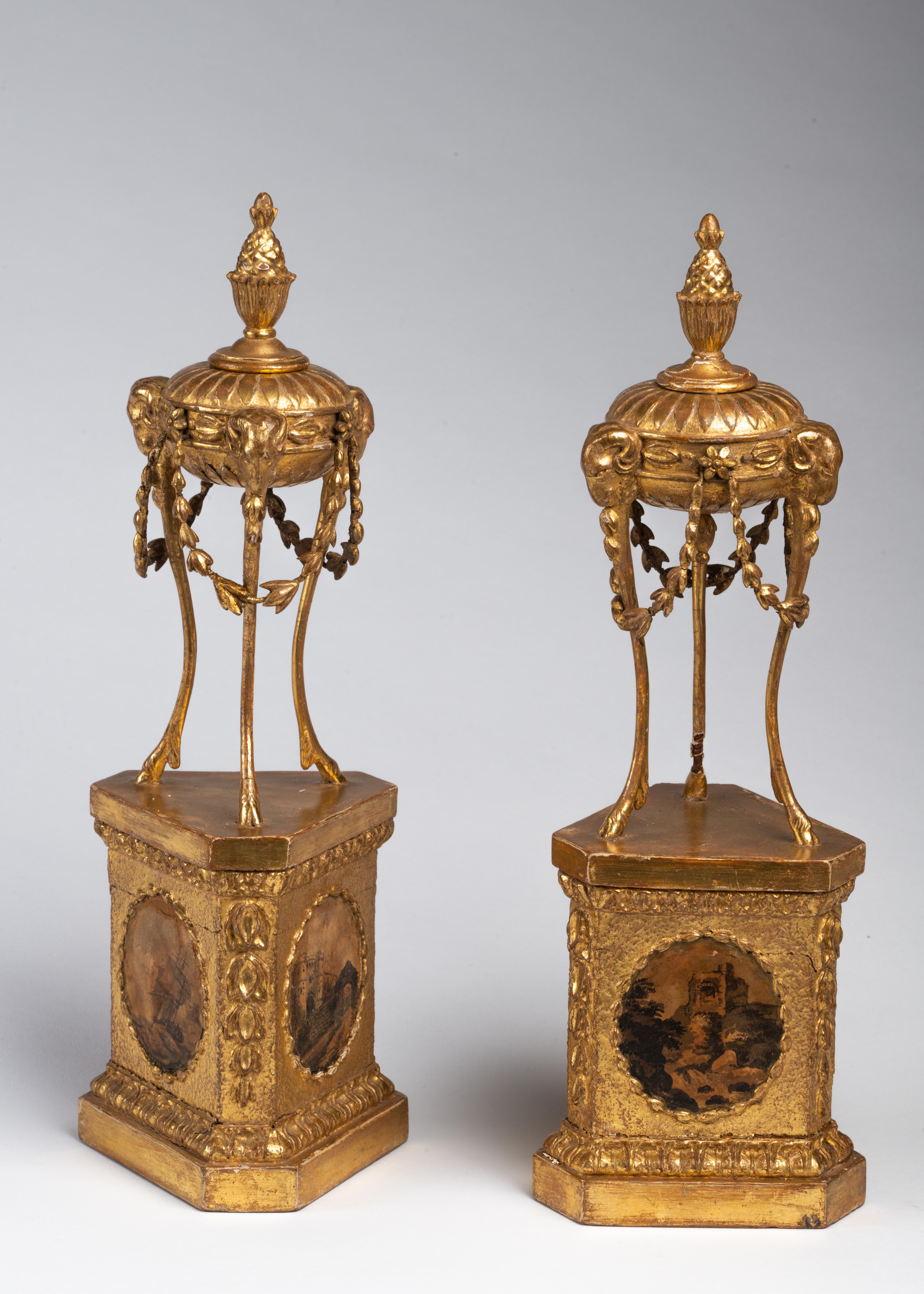 Each in the form of an antique tripod topped with a pineapple finial, draped in floral swags and supported by three ram masks terminating in hoof feet, mounted on a triangular plinth, each side decorated with oval panels framing miniature paintings