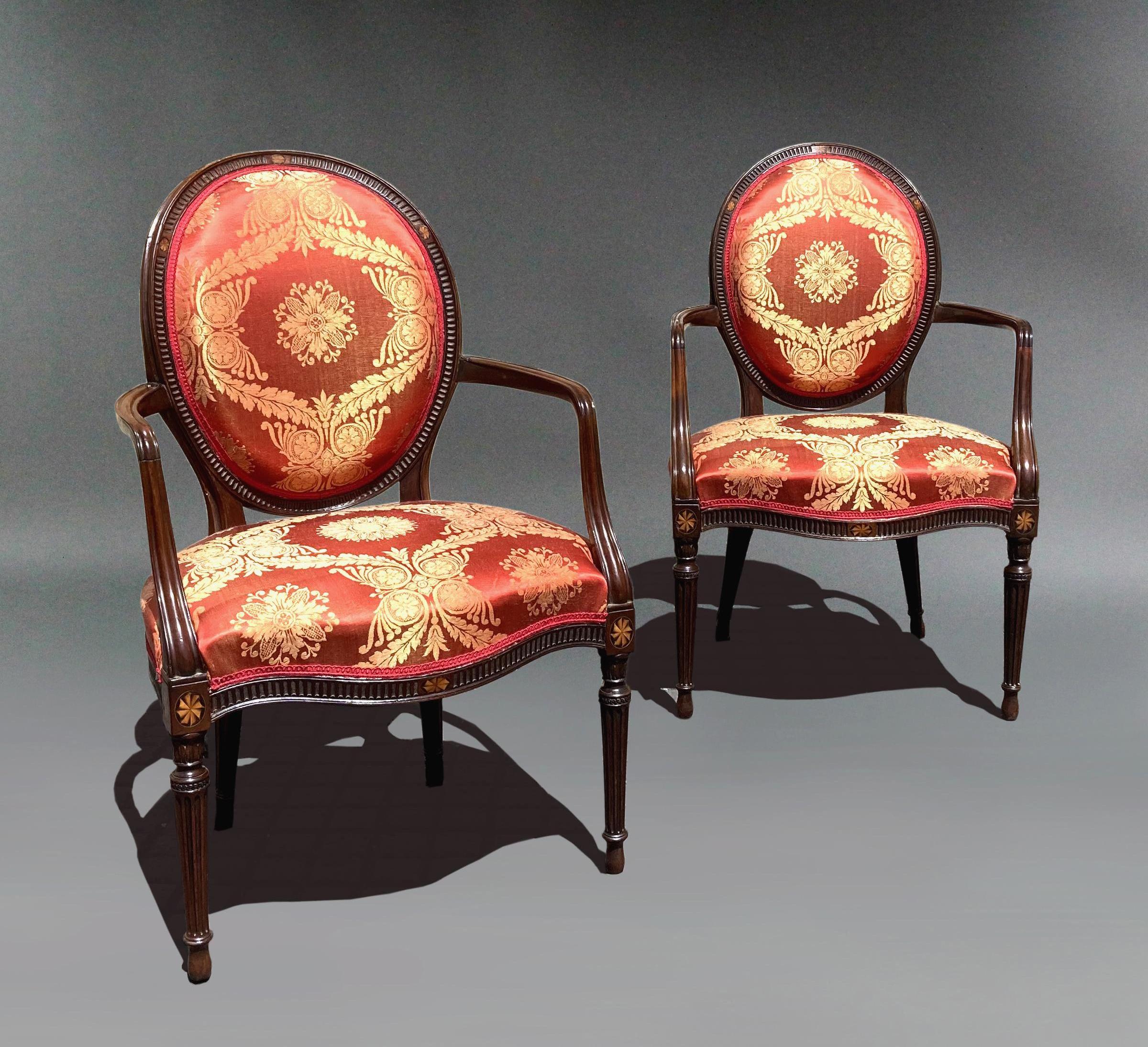 Pair of George III mahogany armchairs in red damask; manner of John Linnell.
The upholstered backs and seats are covered in red silk damask and joined by scrolled arms. The serpentine rails and oval backs with carved fluted detail and with