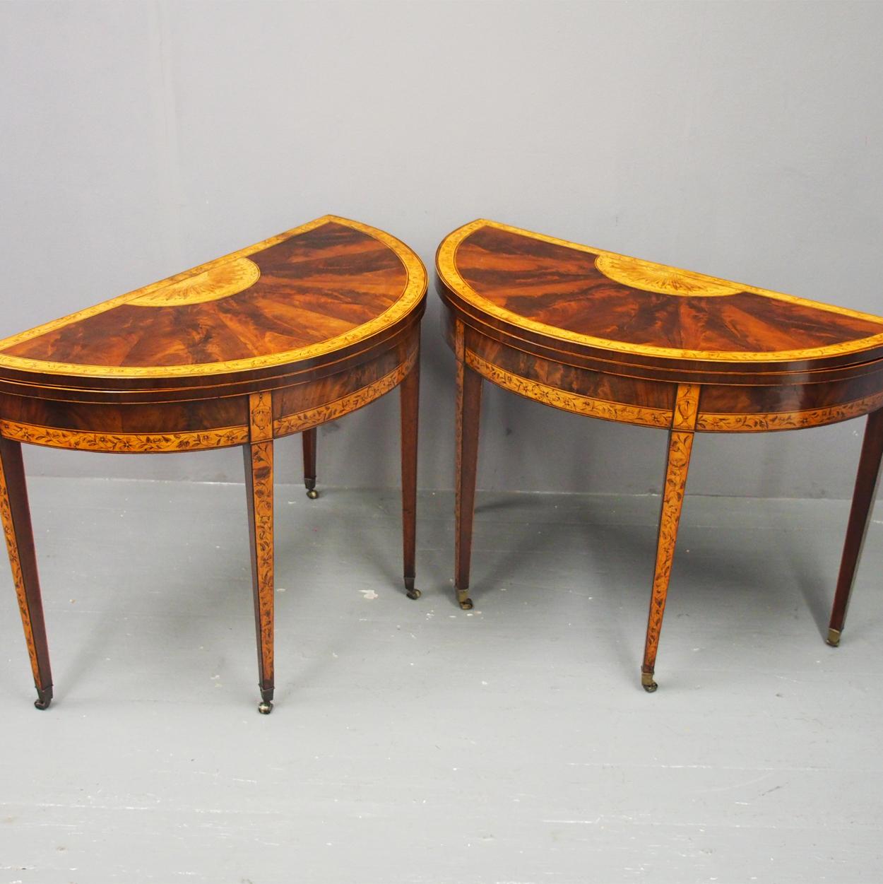 Pair of George III mahogany inlaid and penwork demilune games tables, circa 1770. With their fold over tops and radial veneers centred by a sunflower motif and banding with flower trails. Opening to green baize surfaces, and raised on square