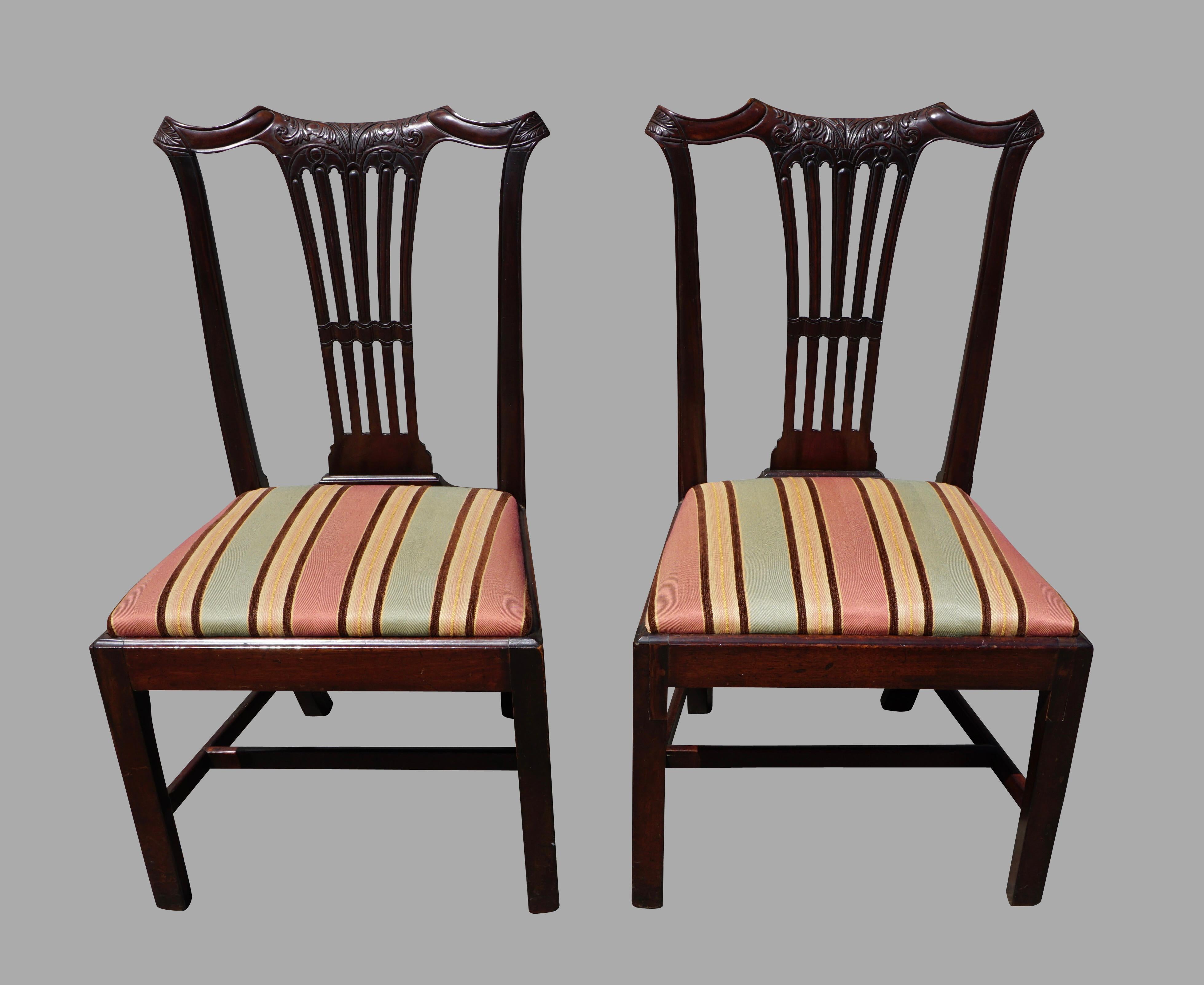 A pair of English Georgian late 18th century mahogany side chairs, each with a shaped and well-carved crestrail over a carved central open splat, the drop in seats covered in striped fabric all supported by square legs. These chairs have good scale,