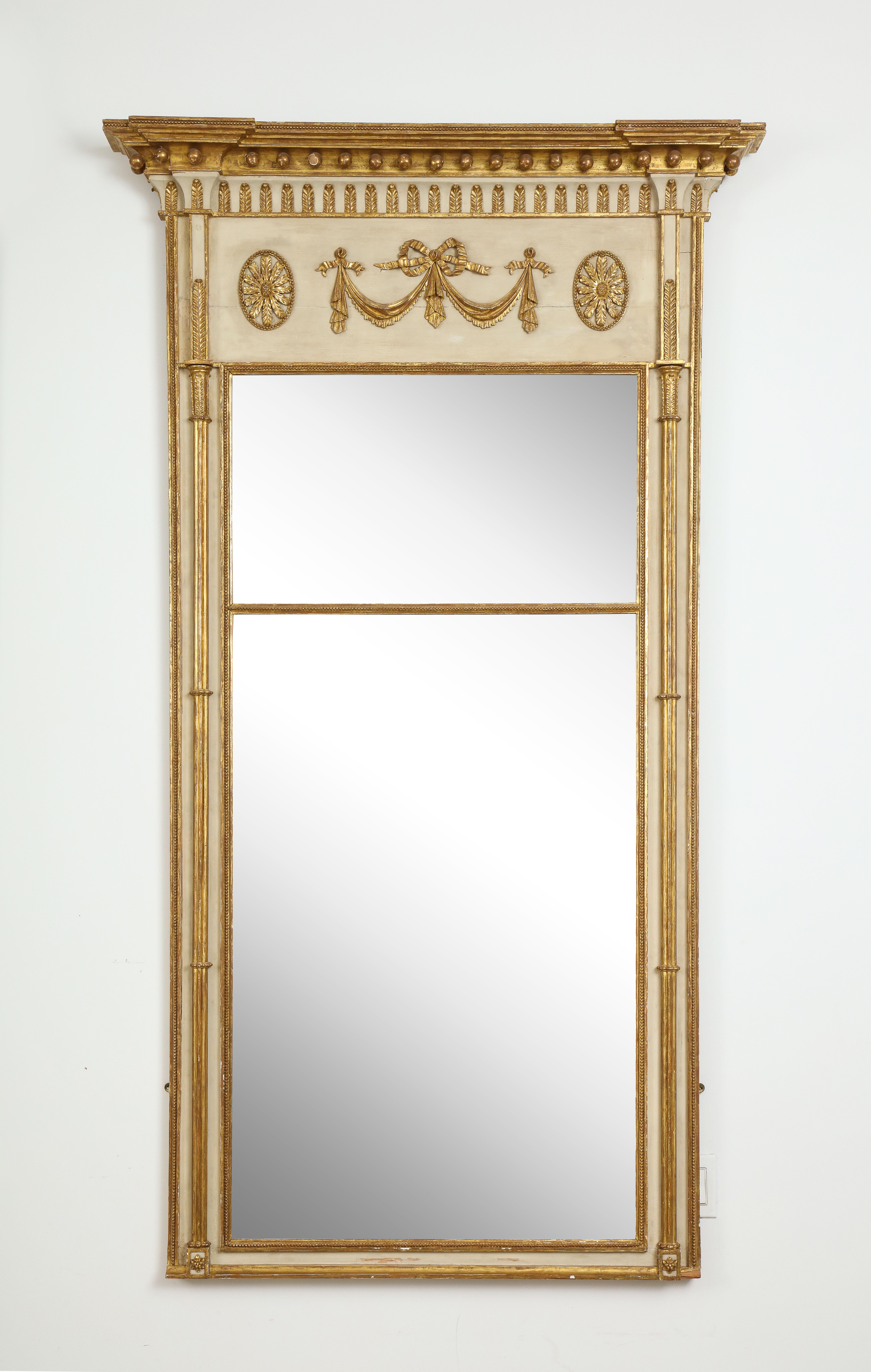 Of elegant architectural design and finely articulated ornament. The divided rectangular mirror plates set between gilt cluster columns, and surmounted by an ivory-painted frieze with gilt ribbon-tied swags between two oval flowerheads below a