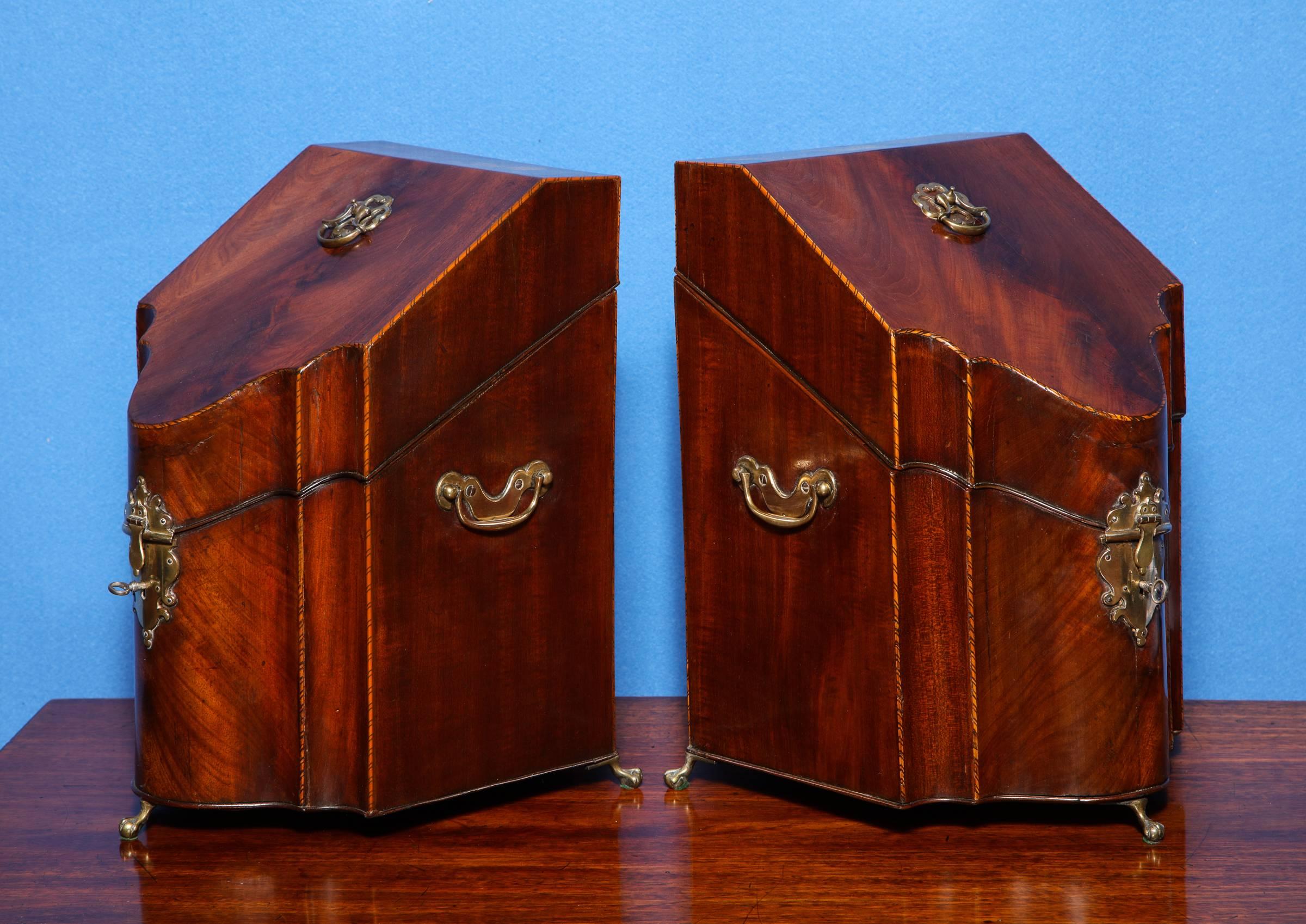 Fine pair of George III period serpentine mahogany knife boxes, with checkered stringing and original brass handles and elaborate escutcheons and ring handles, and having brass ball and claw feet. The hinged top opening to interiors fitted for