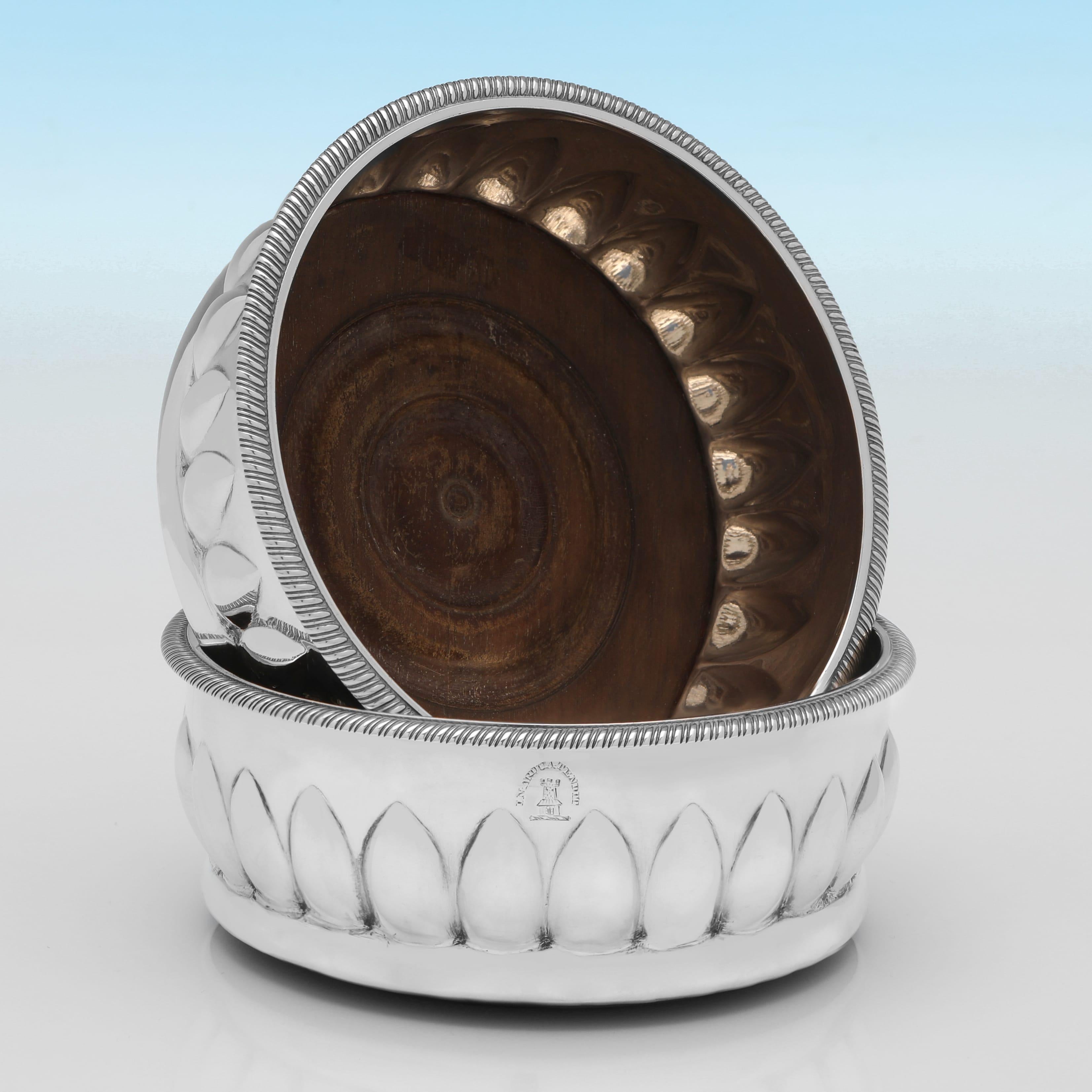Poinçonnée à Londres en 1802 par Solomon Hougham, cette élégante paire de sous-verres en argent sterling ancien de la période George III présente des bases en bois, des bordures à godrons, des bandes de feuilles de lotus stylisées et en relief,