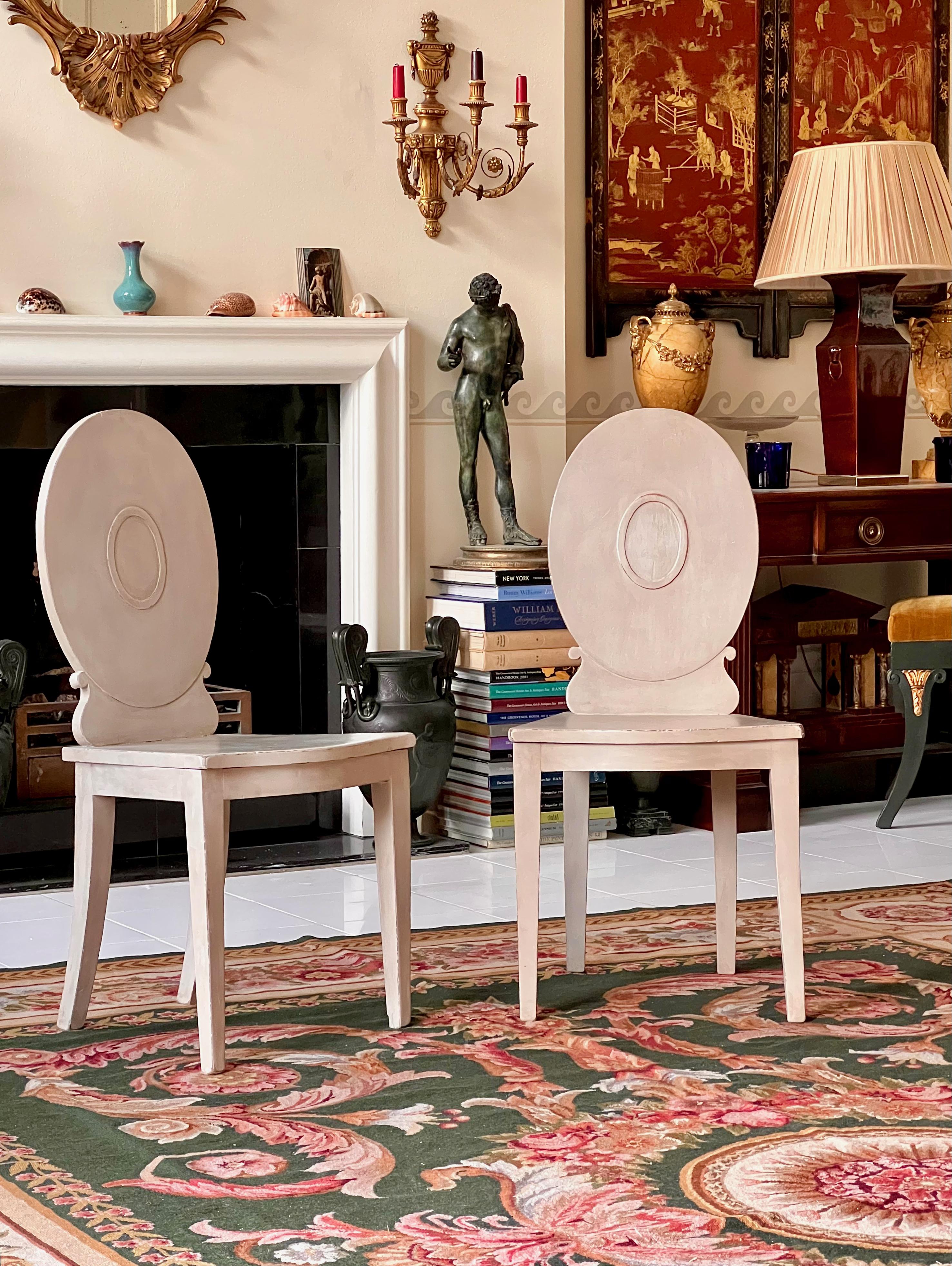 A charming pair of George III period grey-painted hall chairs
England, circa 1795.

Why we like them
Their spartan design, being essentially an iconic neoclassical oval back reduced to the very basics, is beautifully complemented by their