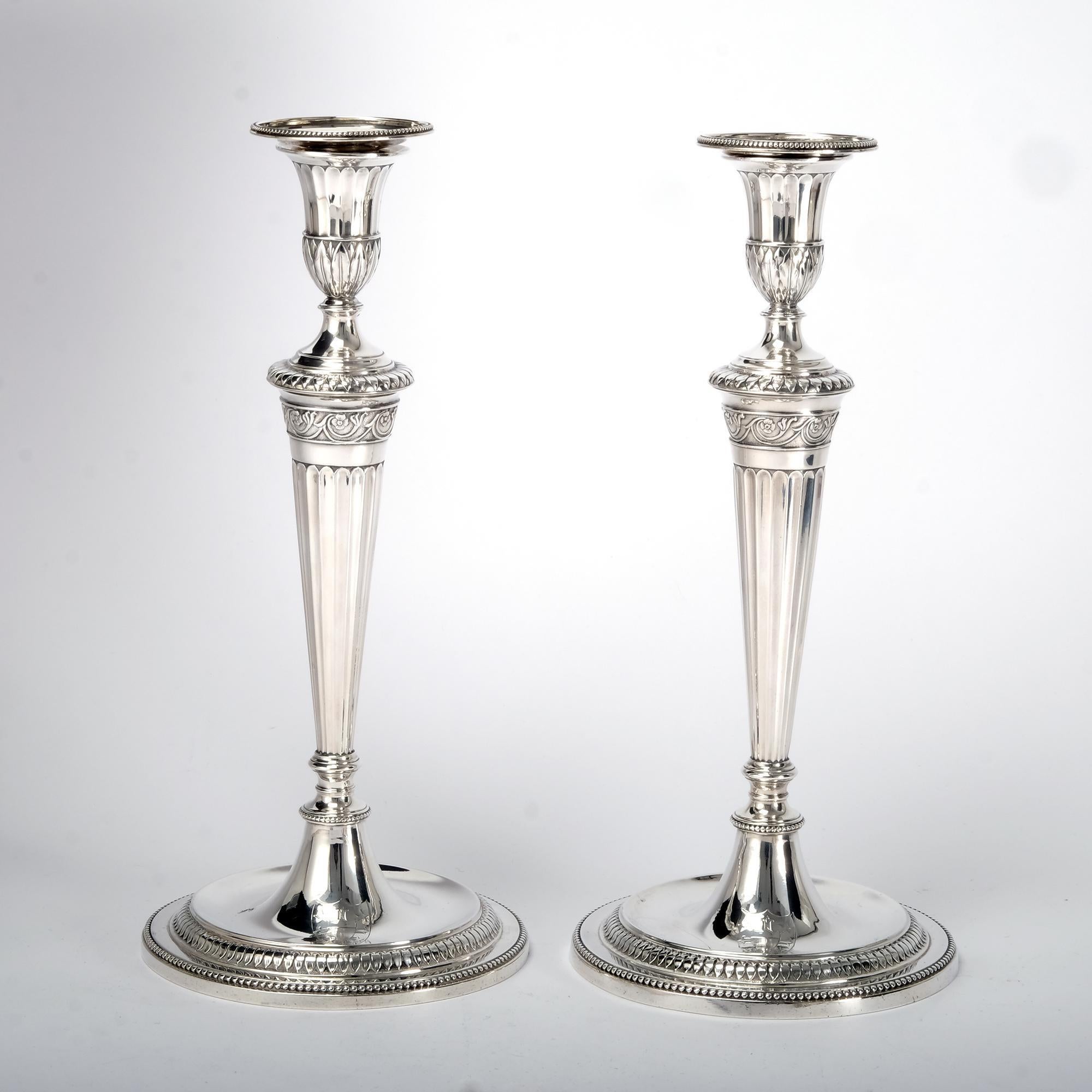 Exceptionally fine pair of antique George III silver candlesticks. Each candlestick has a round sunken well base with beaded border and a band of leaf decoration. The tapering stems are fluted and feature a band of neoclassical-style leaf and flower