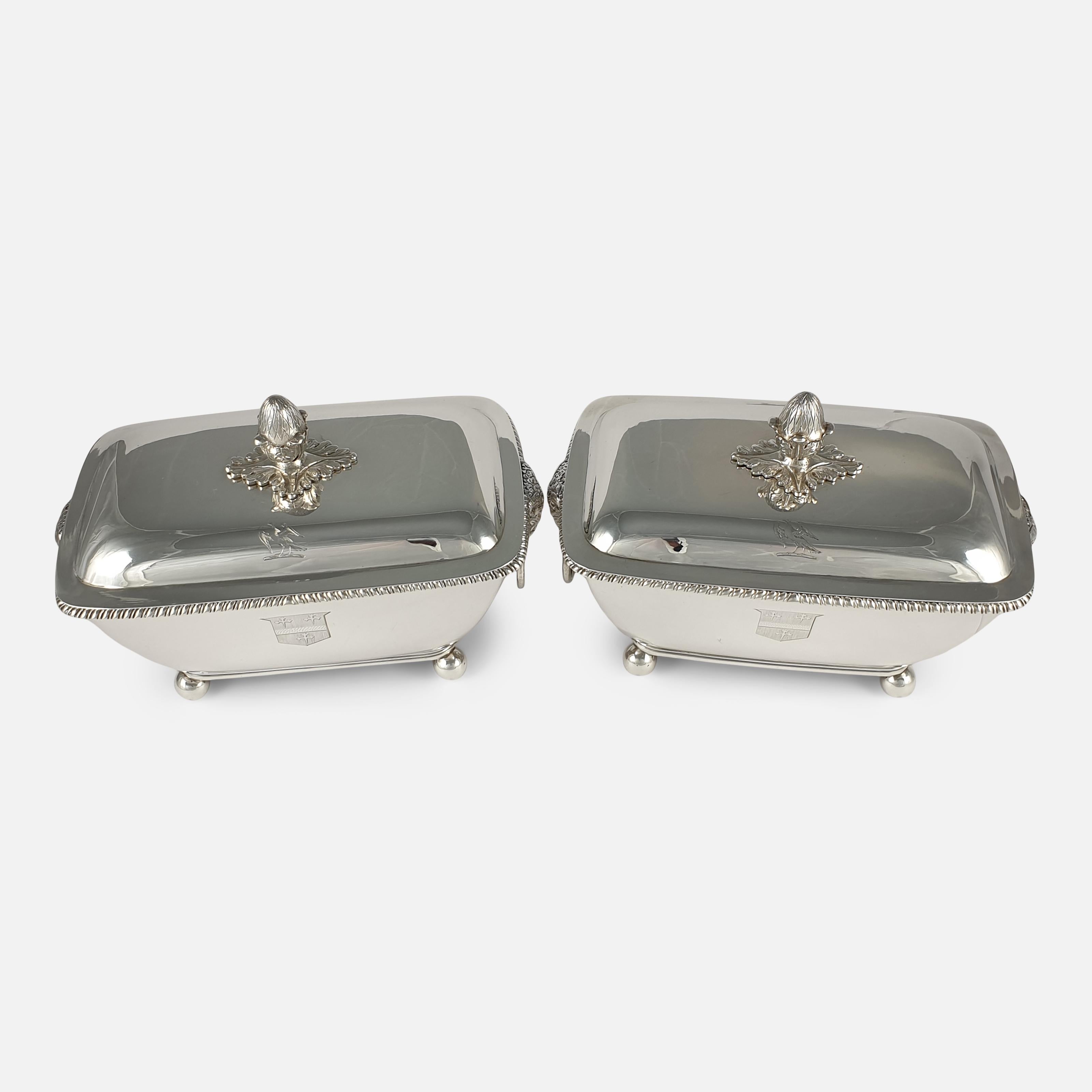 A pair of George III silver rounded rectangular sauce tureens and covers by John Robins, London, 1802. The pair of tureens are set with acorn finials to the shallow domed covers, having twin ram's mask ring handles, and are both engraved with a