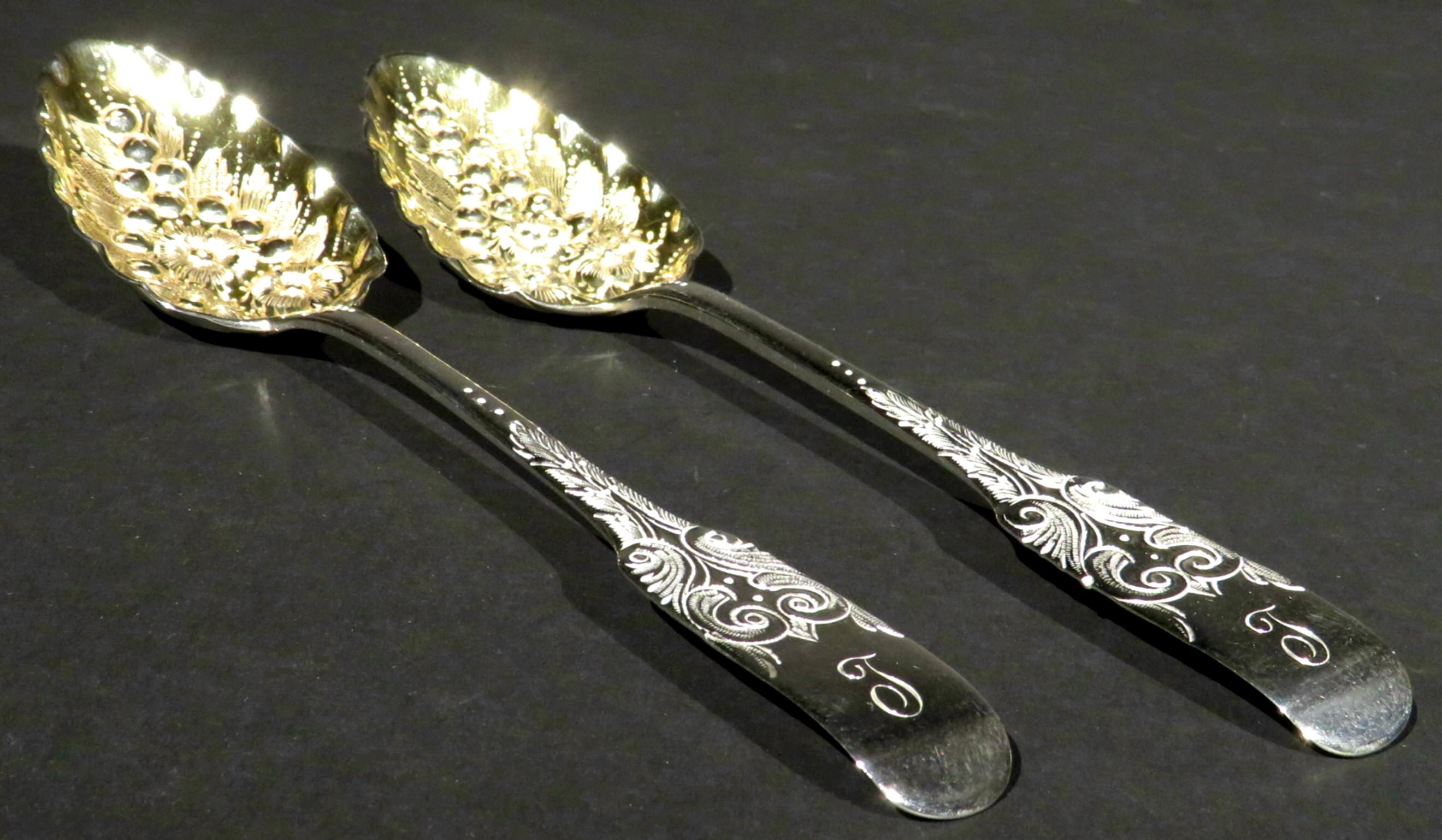 An exceptionally fine pair of early 19th century George III sterling silver berry spoons in the fiddle pattern, both showing richly gilded bowls embossed with motifs of berries & foliage, the handles engraved with scrolls and bright-cut detail.