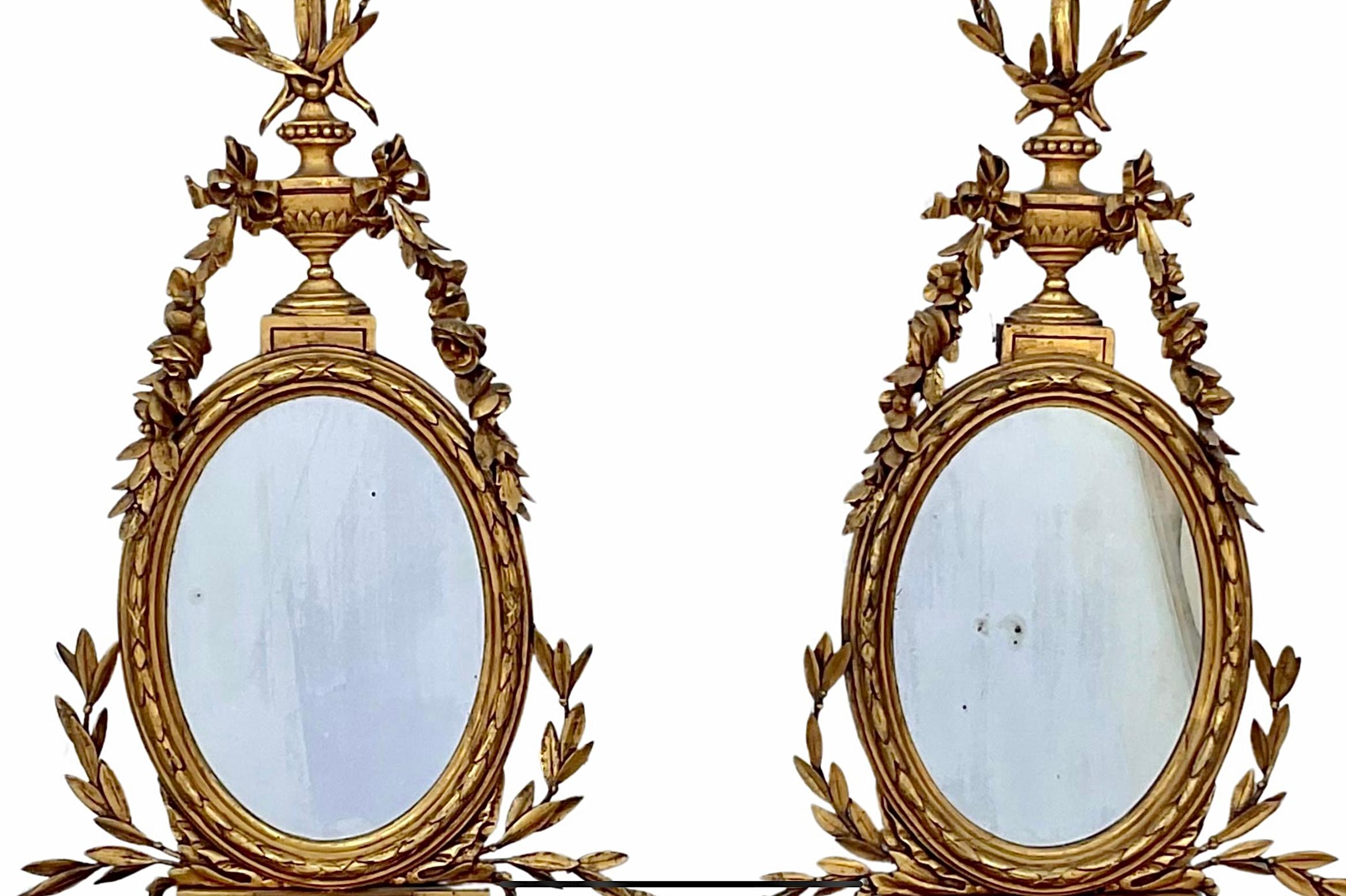Paar Wandhalterungen aus Giltwood und Girandole im Stil von George III. aus dem 19. Ein goldenes Band und eine goldene Schleife über einer geschnitzten Urne mit Goldfolie, die bis zu einem ovalen Spiegel über einem urnenförmigen Wandregal reicht.