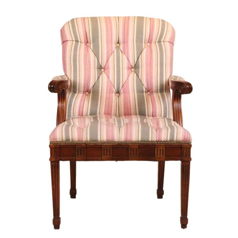An early 20th century pair of George III style tufted armchairs with curved arms ending in scroll shape, with both carved, reeded design and upholstered arm rests. Chair back is curved and legs are straight and fluted with a decorative, alternating