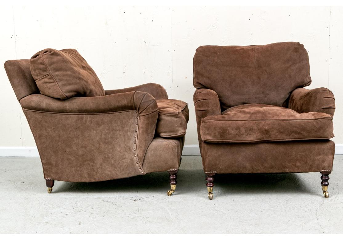 Pair of George Smith brown suede leather signature lounge chairs with rolled English arm and feather and down cushions. The chairs with loose pillow back and seat, turned front legs and tapering back legs all with brass casters. Brass nail head