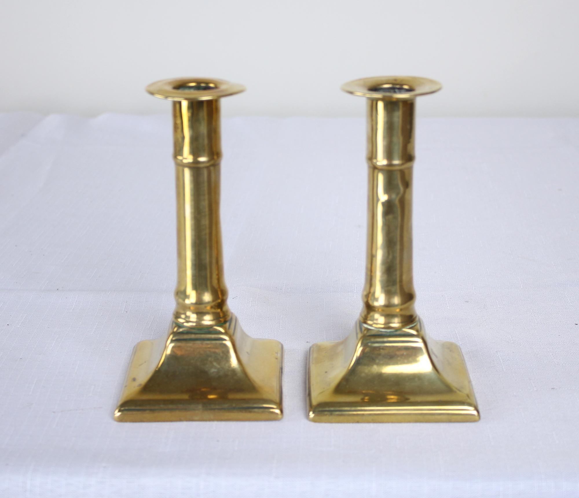 A pair of antique English brass candlesticks, from the Georgian period. Note that they need to be properly positioned, facing front, to look straight. This is a peculiarity on some Georgian candlesticks that were going onto a mantle and would tilt