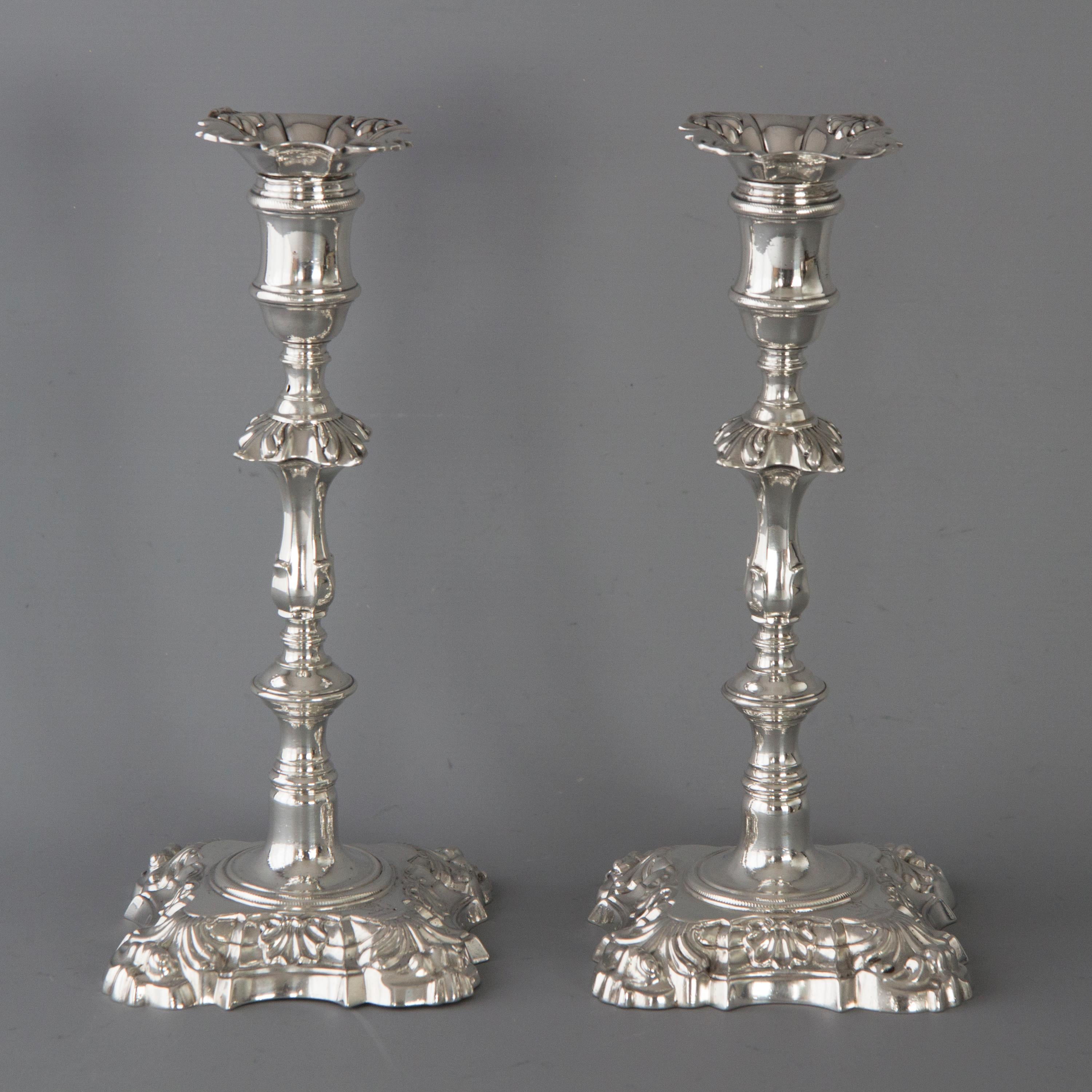 A very good pair of George III cast silver table candlesticks of shell and scroll decoration to a square shaped base. The stem with a circular knop and a fluted rectangular knop. Rope twist decoration to the base and capitals. Conforming shell