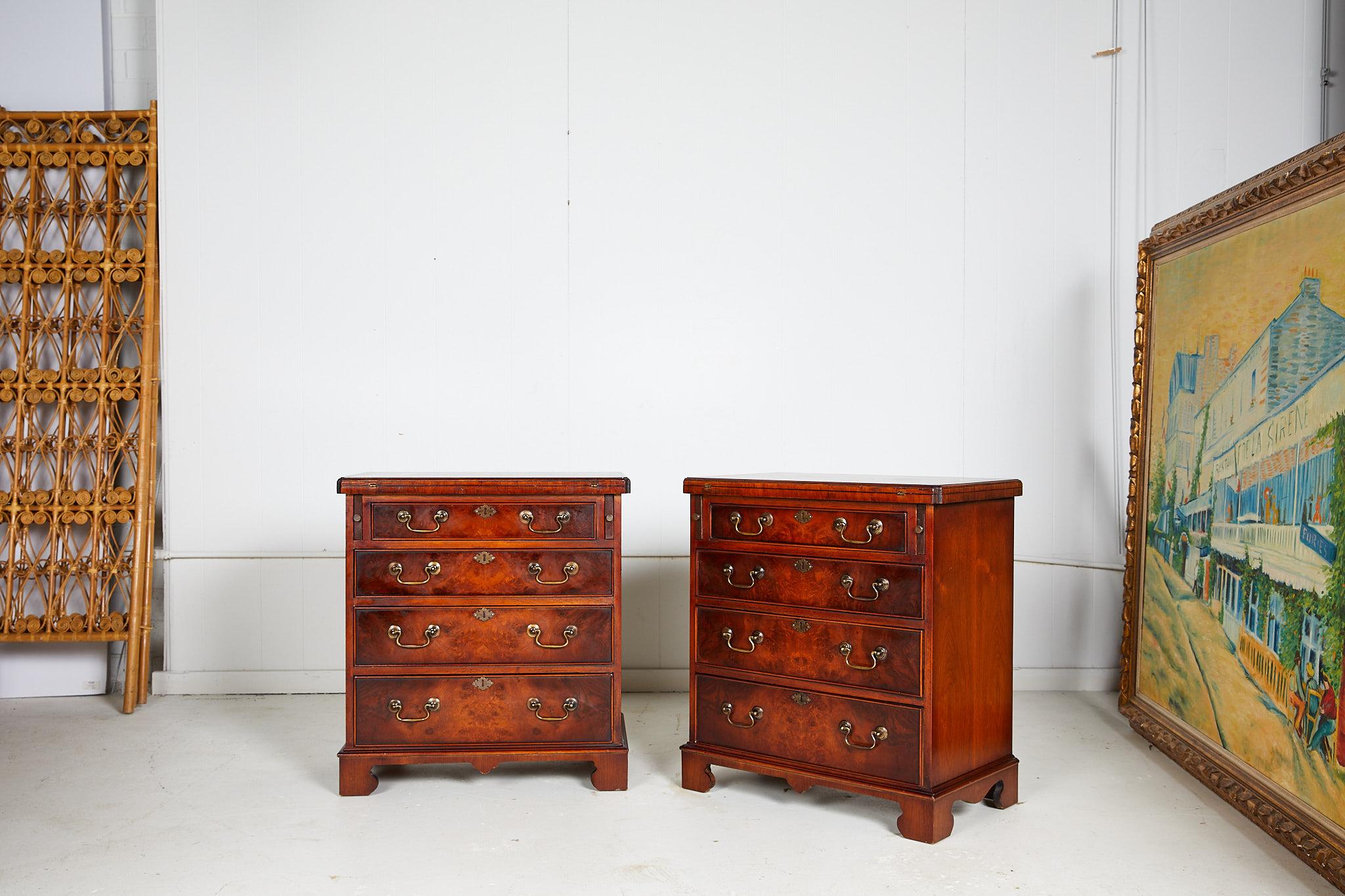 20th century petite pair of Georgian style bachelor's chests beautifully veneered in mahogany and burl walnut with feather banded details on the table top. The chests feature a shaped fold over rectangular top supported by two pull-out slides (which