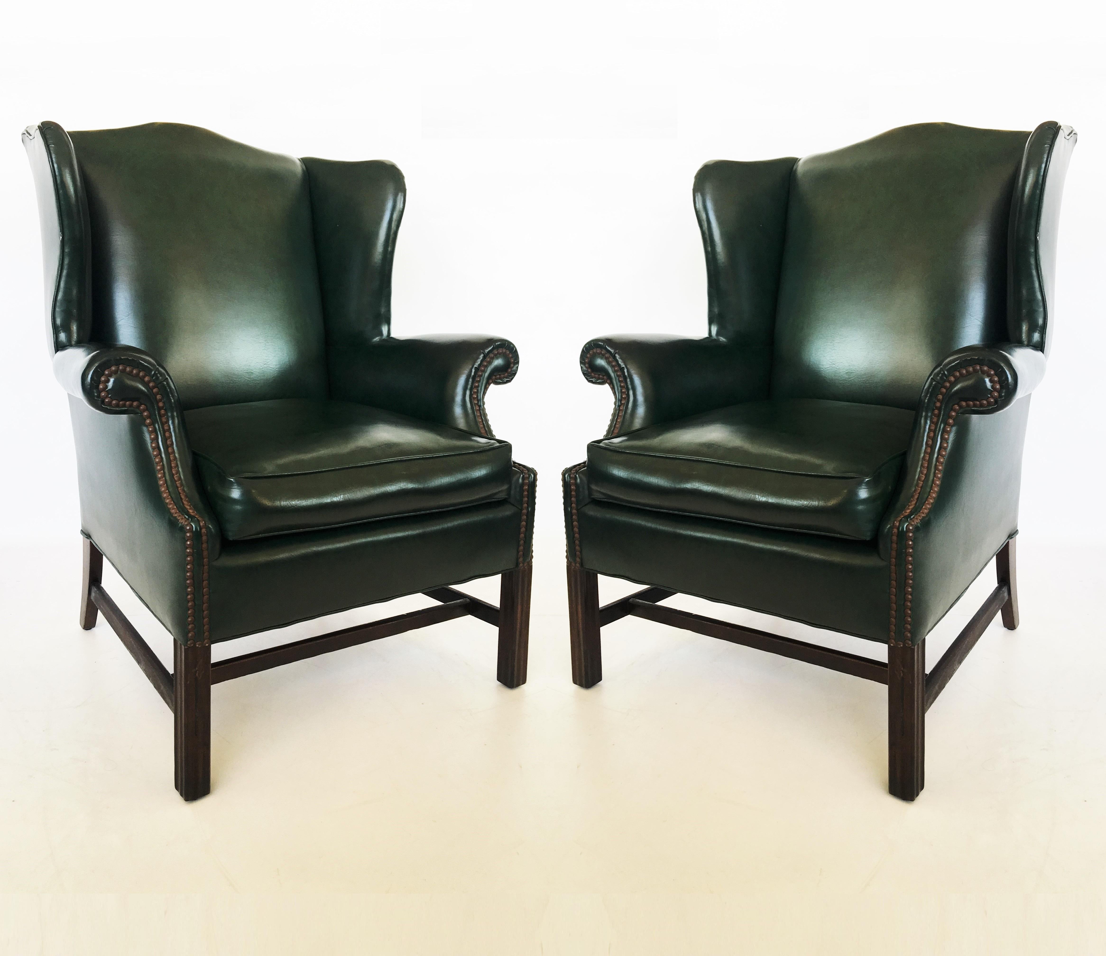 An extraordinary and comfortable pair of early to mid-20th century Georgian forest green leather wingback armchairs. Each chair features a domed crest rail, wing panels, rolled armrests and loose cushioned down seat. The brass stud work to the front