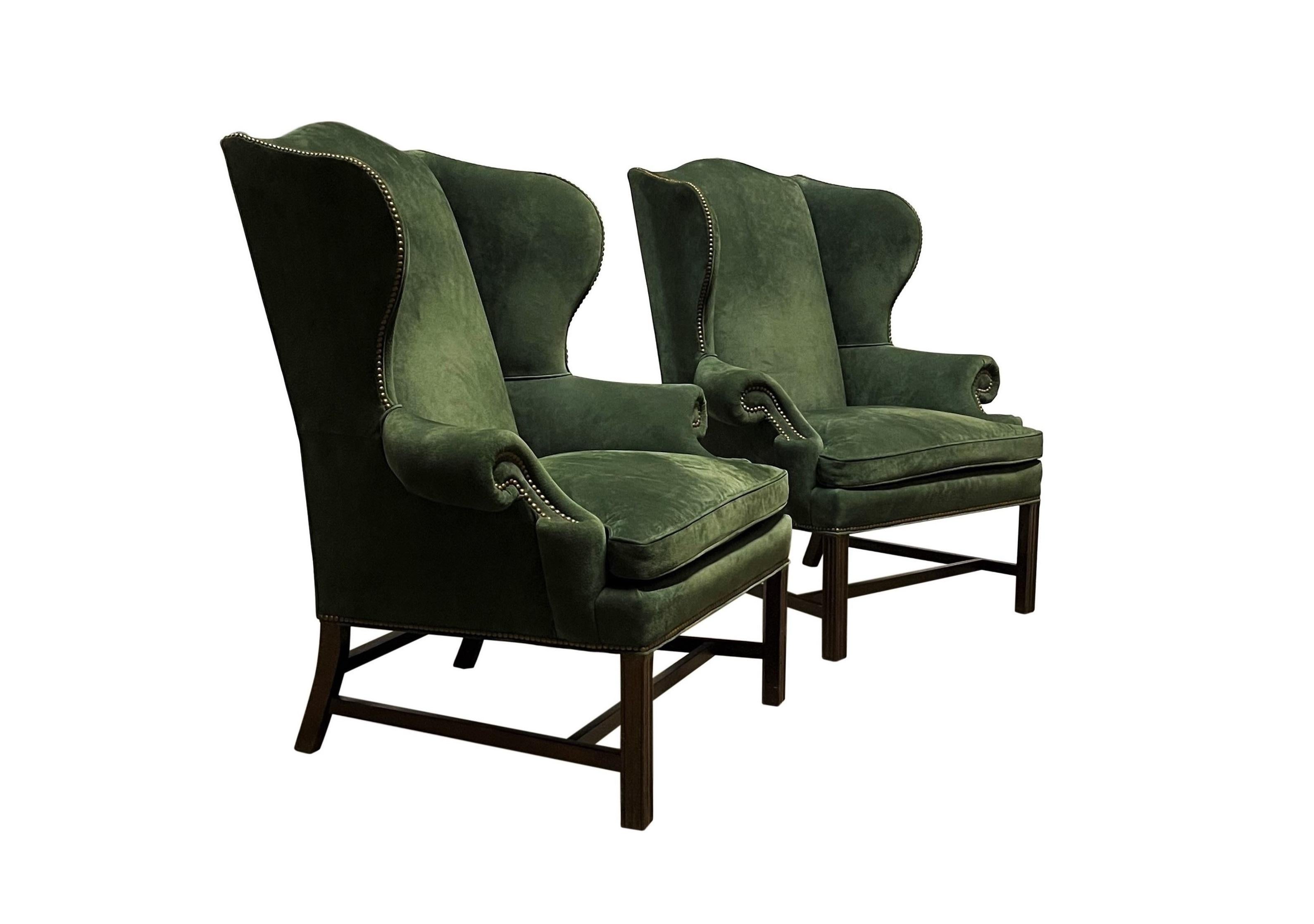 An extraordinary and comfortable pair of early to mid-20th century Georgian green suede leather wingback armchairs. Each chair features a serpentine-shaped crest rail, wing panels, rolled armrests and loose cushioned down seat. Richly detailed, the