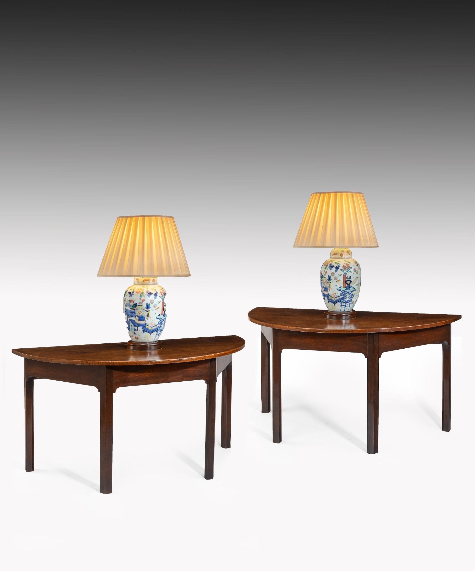 A handsome pair of George III Chippendale period mahogany demilune console tables; the well figured mahogany top above a crossgrain veneered frieze and raised on square moulded legs.

This pair of console tables were originally the D-ends of a