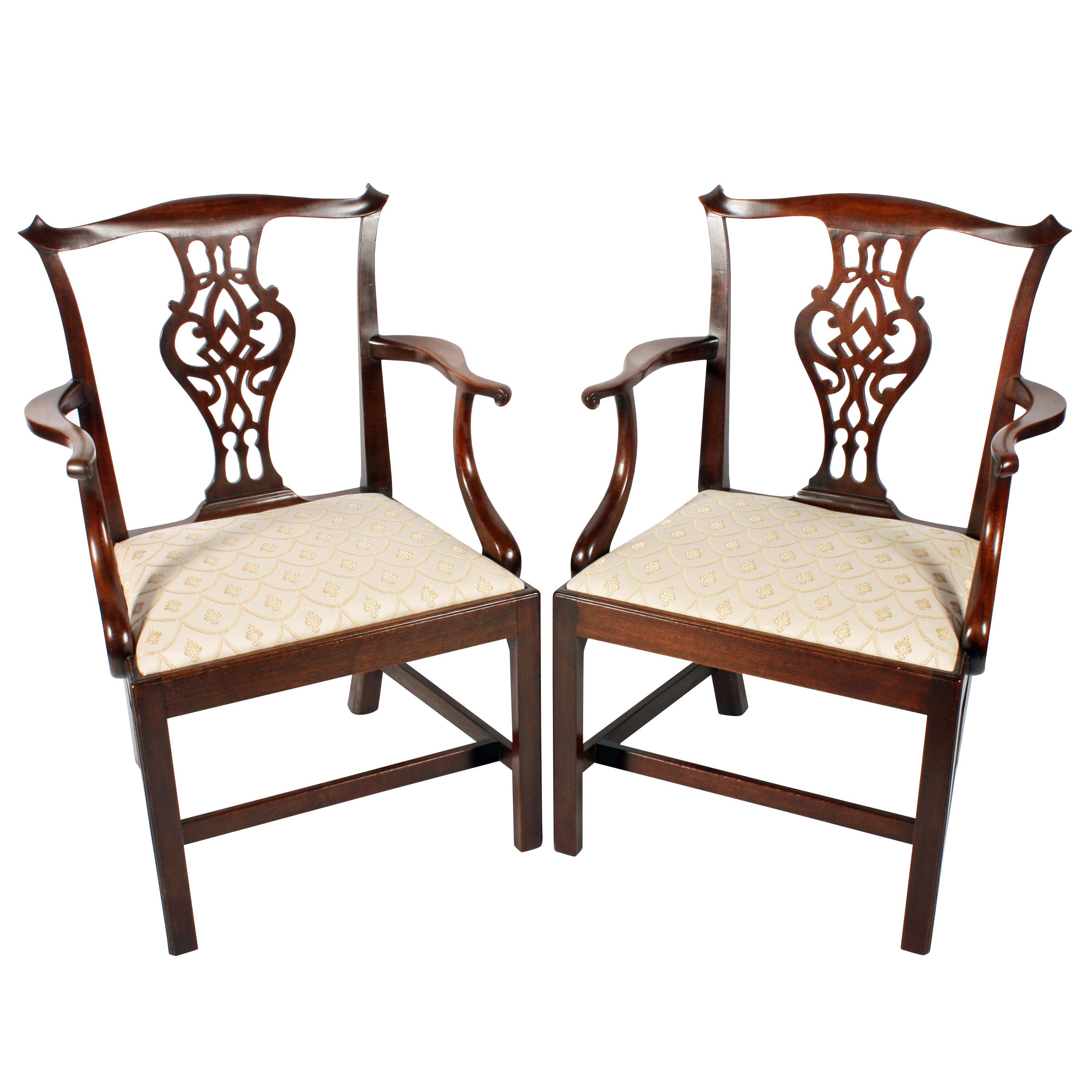 A pair of Georgian mahogany elbow chairs of larger proportions.

The chairs have a serpentine top rail with concave scroll ends and drop in pad seats.

The broad centre splat is fret work carved, the shaped arm rests have a carved support and a
