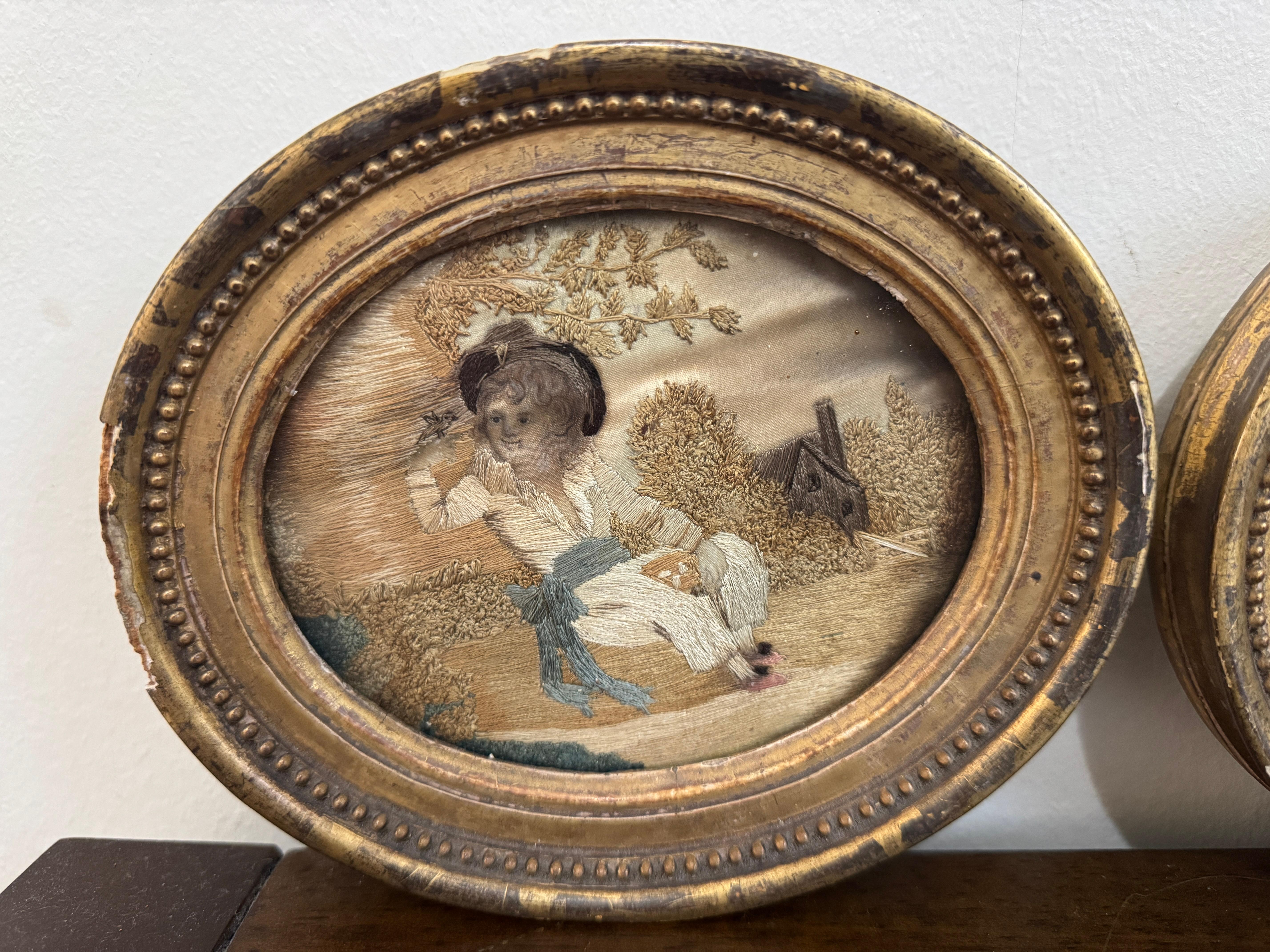 Ein Paar georgianischer handgestickter ovaler Seidentafeln, um 1800, eine zeigt einen sitzenden Jungen mit einem Vogel, die andere ein Mädchen mit einem Schaf. Beide im Alter von Gold vergoldet verglast Frames, die Größe der jeweils 6,75 