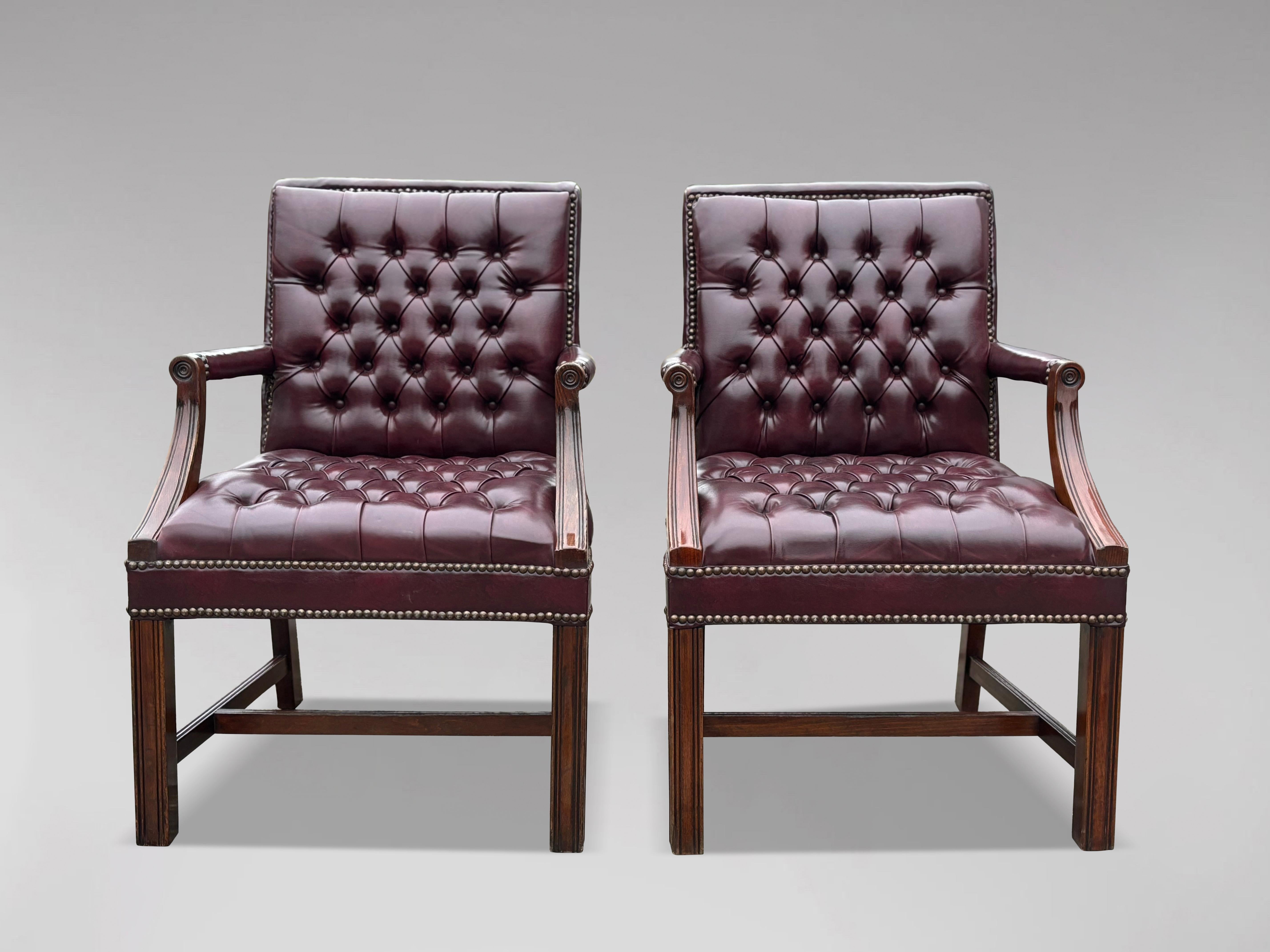 A fine pair of Georgian-style leather Gainsborough library armchairs or desk armchairs, upholstered in deep-buttoned burgundy leather for the backs and seats. The leather upholstery is complemented by brass nail-head trim around the borders.