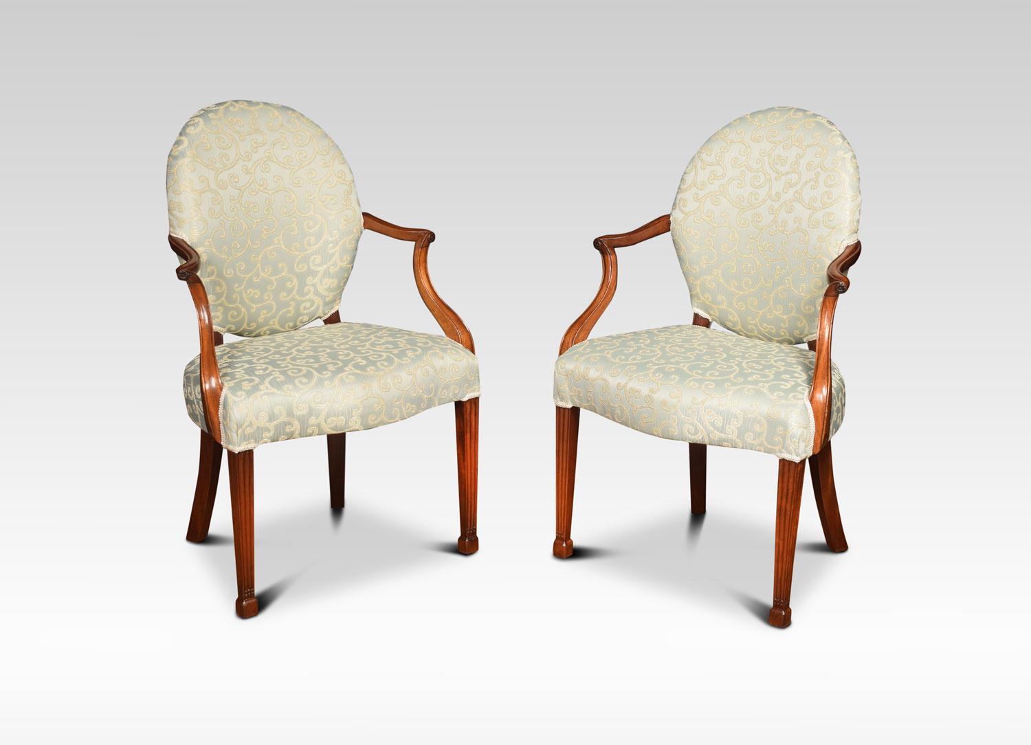 A pair of Georgian style mahogany ladies bedroom armchairs. The oval backs upholstered in pale green silk. Flanked by channeled open arms with carved floret terminals. To the overstuffed serpentine fronted seat. Raised up on fluted square tapering