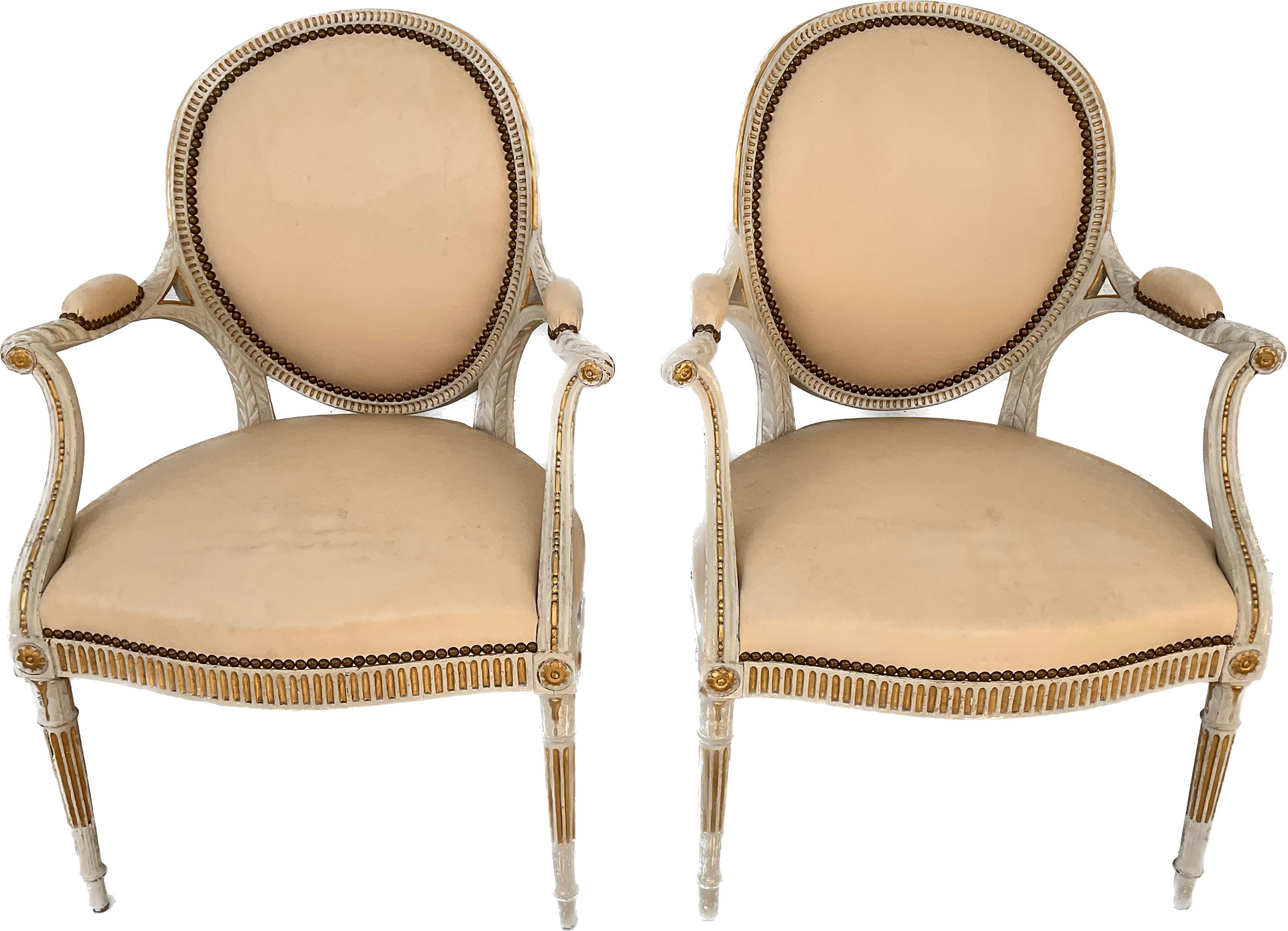 Sophisticated pair of George III style painted armchairs in the Adams taste. Elegant in style in a light cream color, carved painted wood, with gilding and grommets throughout. Back and seat material is soft solid cream leather.