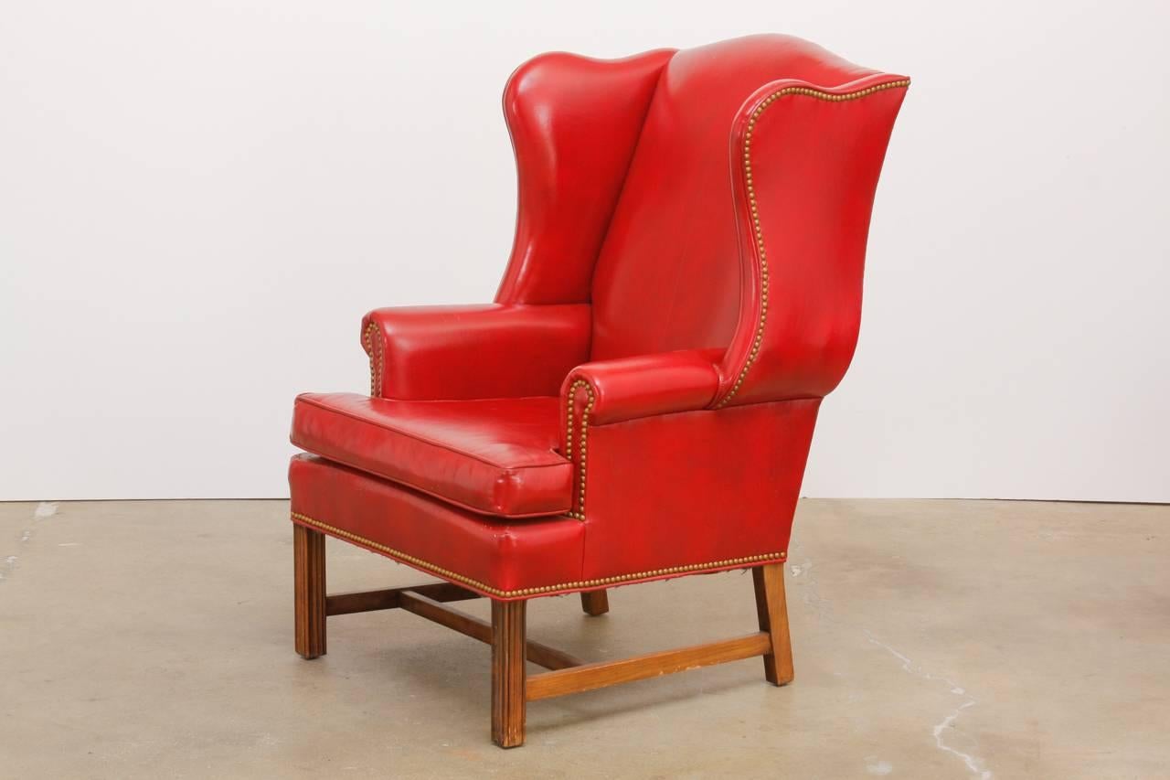 Fantastic pair of red leather wing chairs or library chairs made in the English Georgian taste by Schafer Brothers. Features a mahogany frame covered in smooth red leather accented by brass nail head trim. The wings are fully developed and the