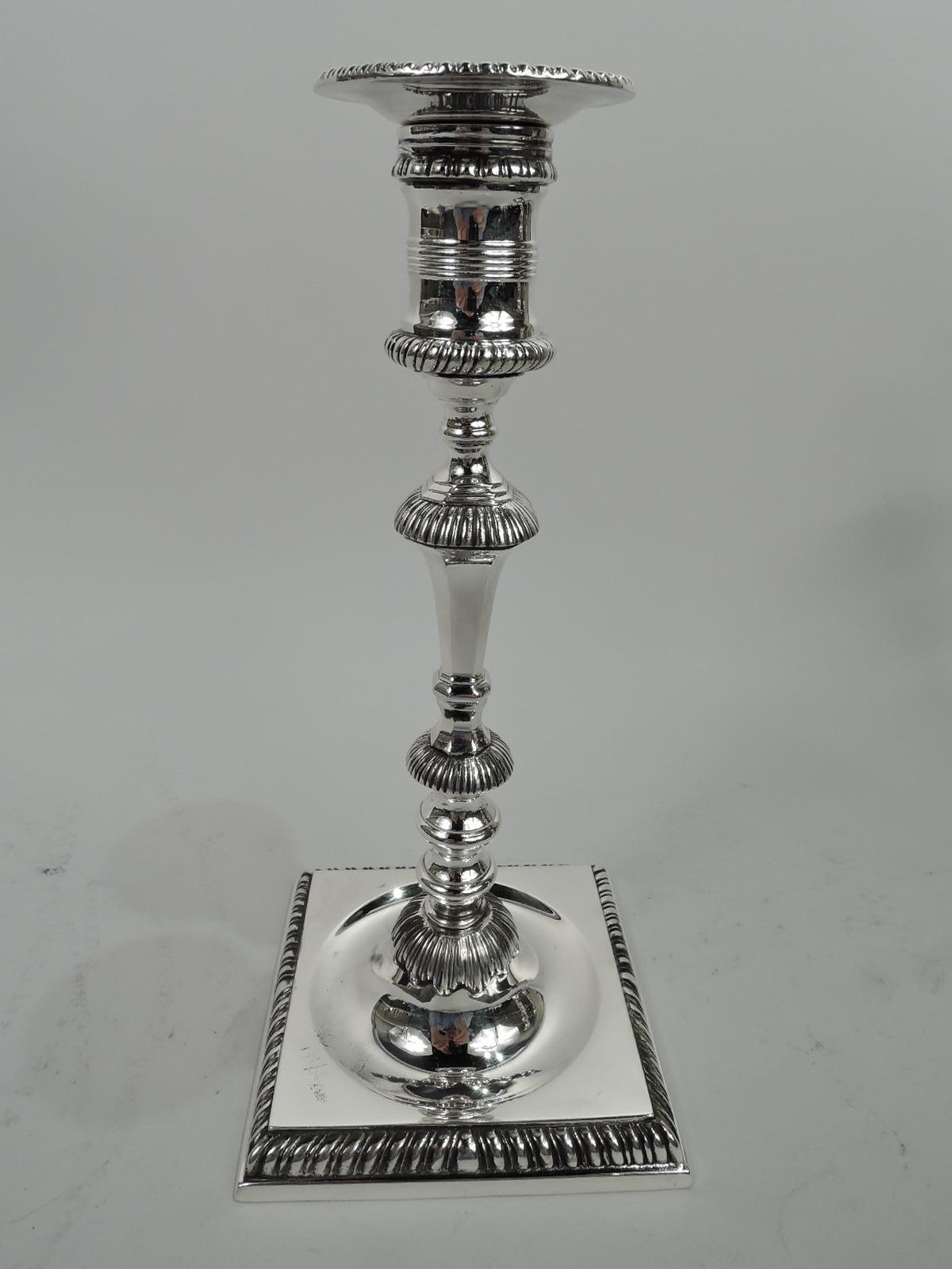 Pair of Georgian-style sterling silver candlesticks. Made by Currier & Roby in New York, ca 1920. Each: Faced and tapering shaft with knops and flanges on raised foot in concave circle set in square base. Spool socket with detachable bobeche.